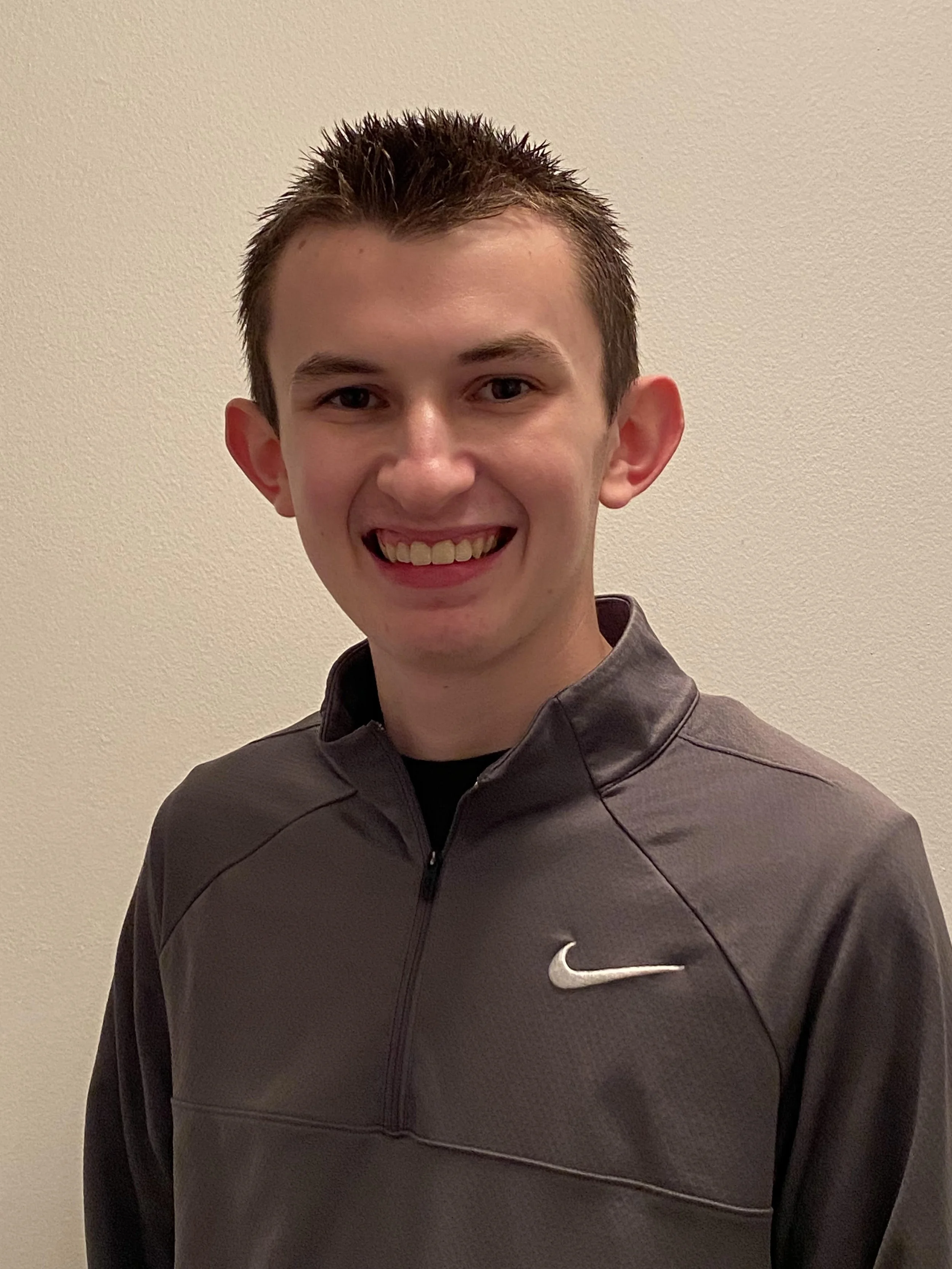 Smiling person in a gray Nike zip-up jacket against a plain background.
