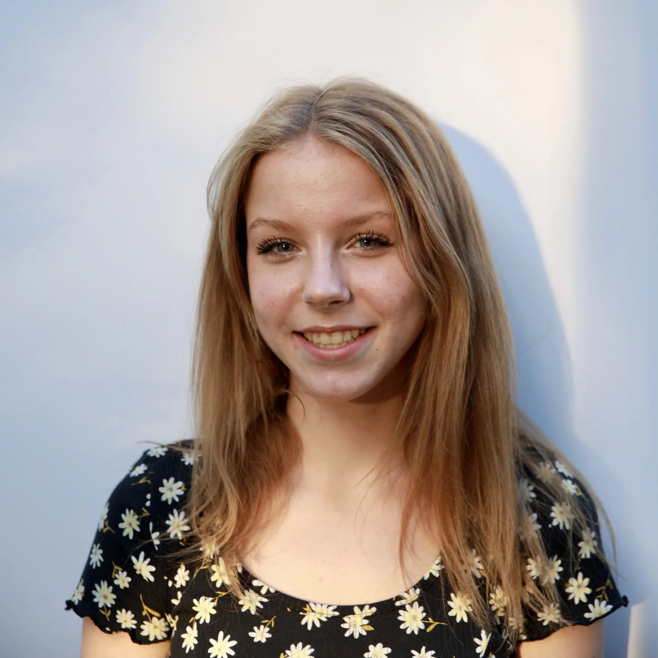 Smiling person with long hair wearing a floral shirt.