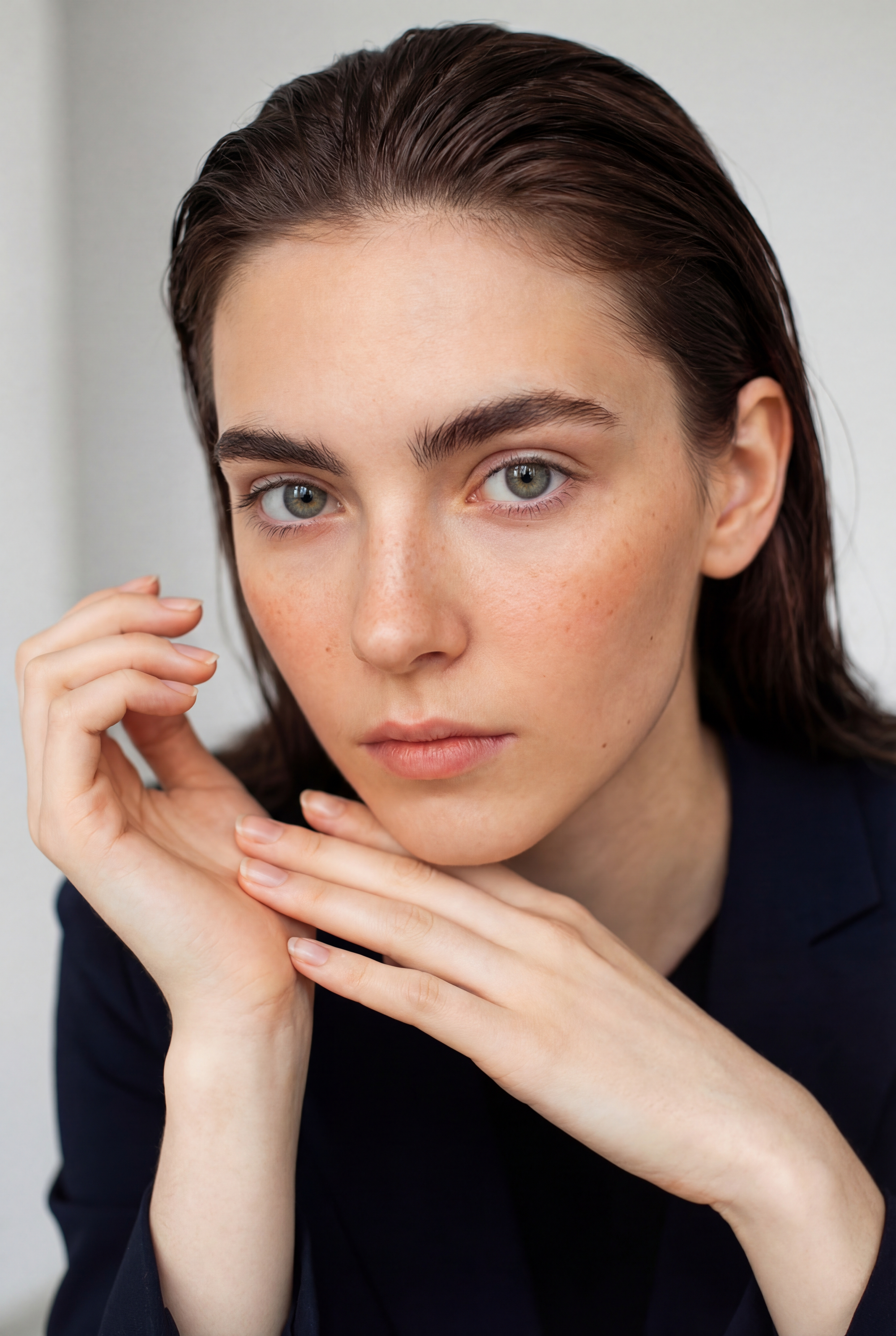 Une femme avec des cheveux bruns, portant une veste noire, regarde fixement l'objectif, avec la main sous le menton.