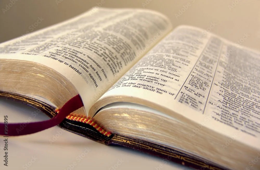 Open Bible with a red and black ribbon bookmark on a white surface.