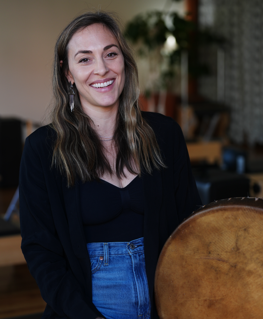 A woman holding a young child stands among flowers and greenery in a garden.