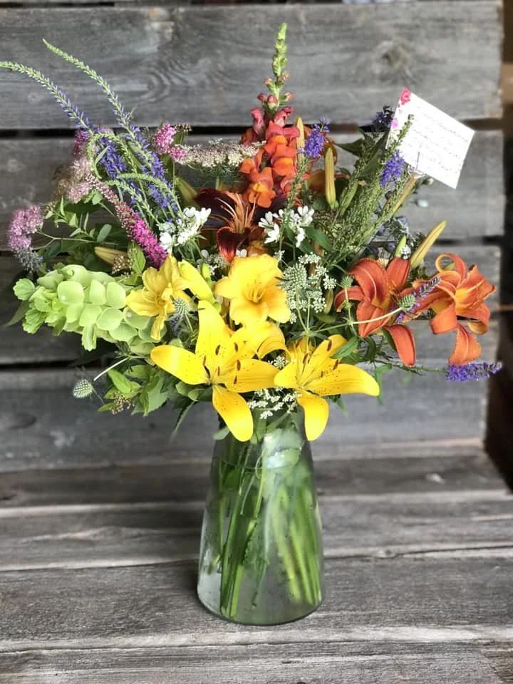 Colorful mixed flower bouquet in a clear glass vase on a wooden surface.