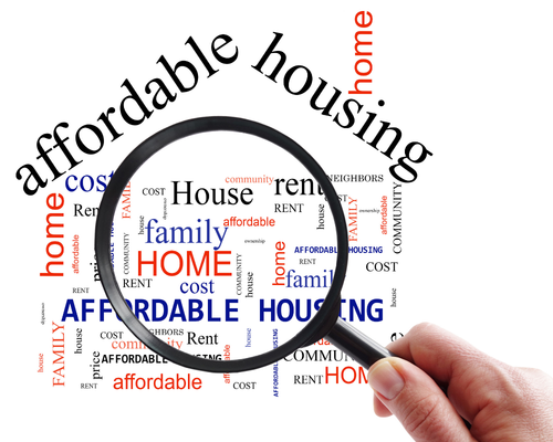 A hand holding a magnifying glass over a word cloud, bringing the words 'affordable housing,' 'family,' and 'home' into clear focus. The surrounding background text includes related terms such as 'cost,' 'rent,' 'community,' and 'neighbors.