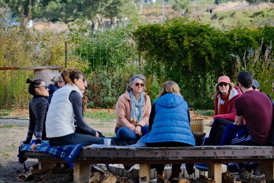 Group of people sitting cross-legged outdoors on a platform, engaging in a discussion or meditation.