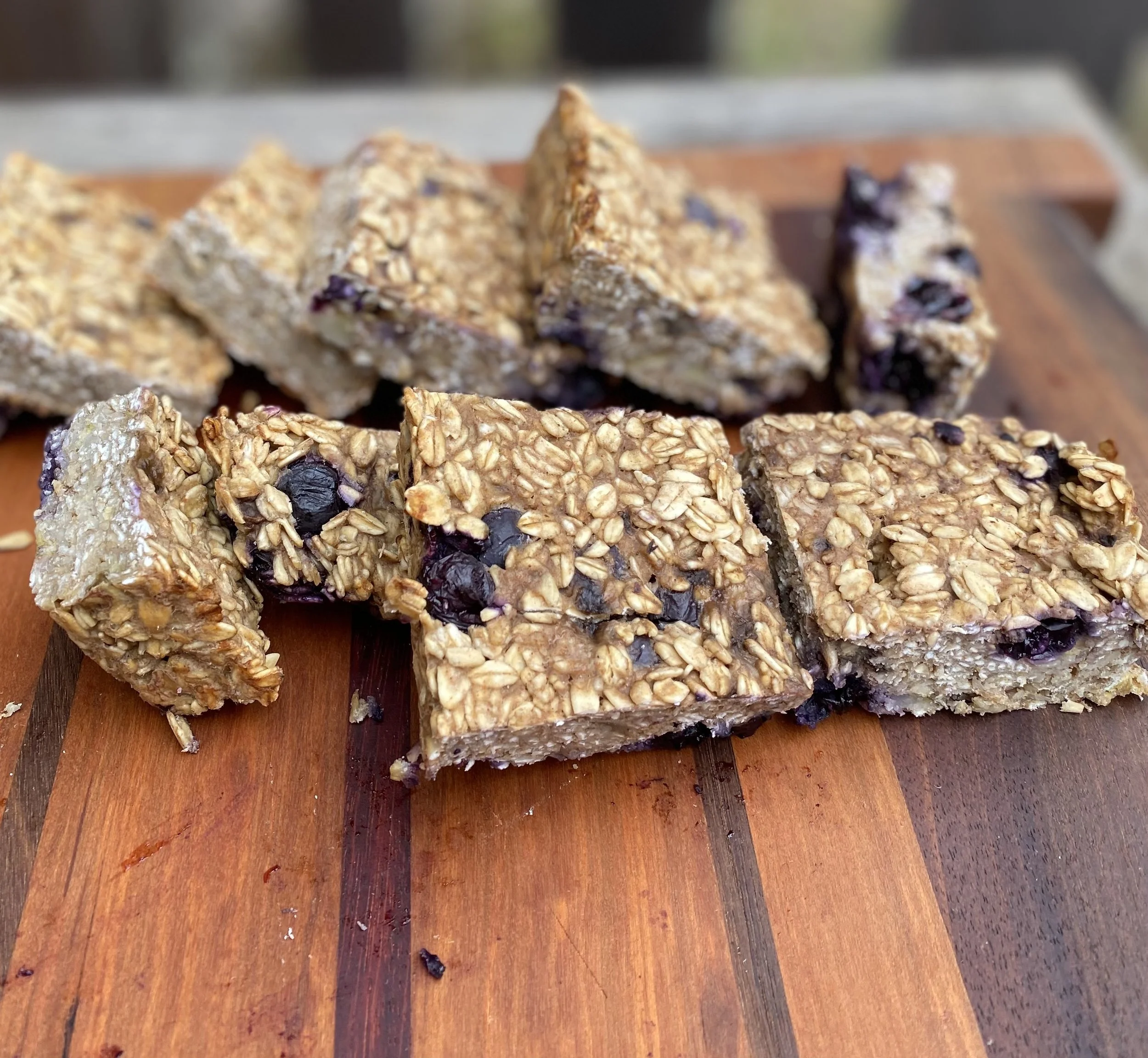 Granola bars with oats and blueberries on a wooden cutting board.