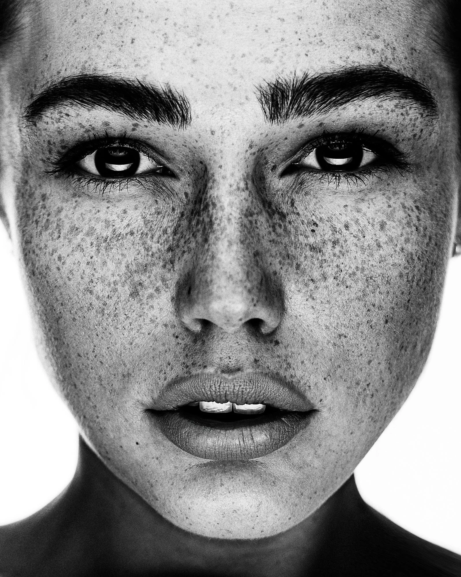 Close-up black and white portrait of a woman with freckles, dark eyebrows, and light eyes.