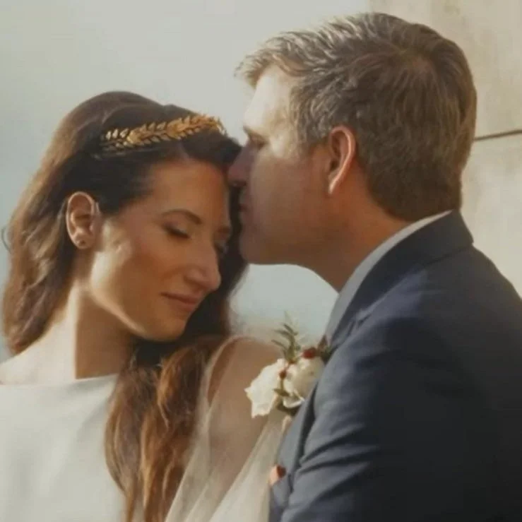 Una coppia di sposi si scambia un gesto affettuoso, con il marito che bacia la moglie sulla fronte durante il loro matrimonio.
