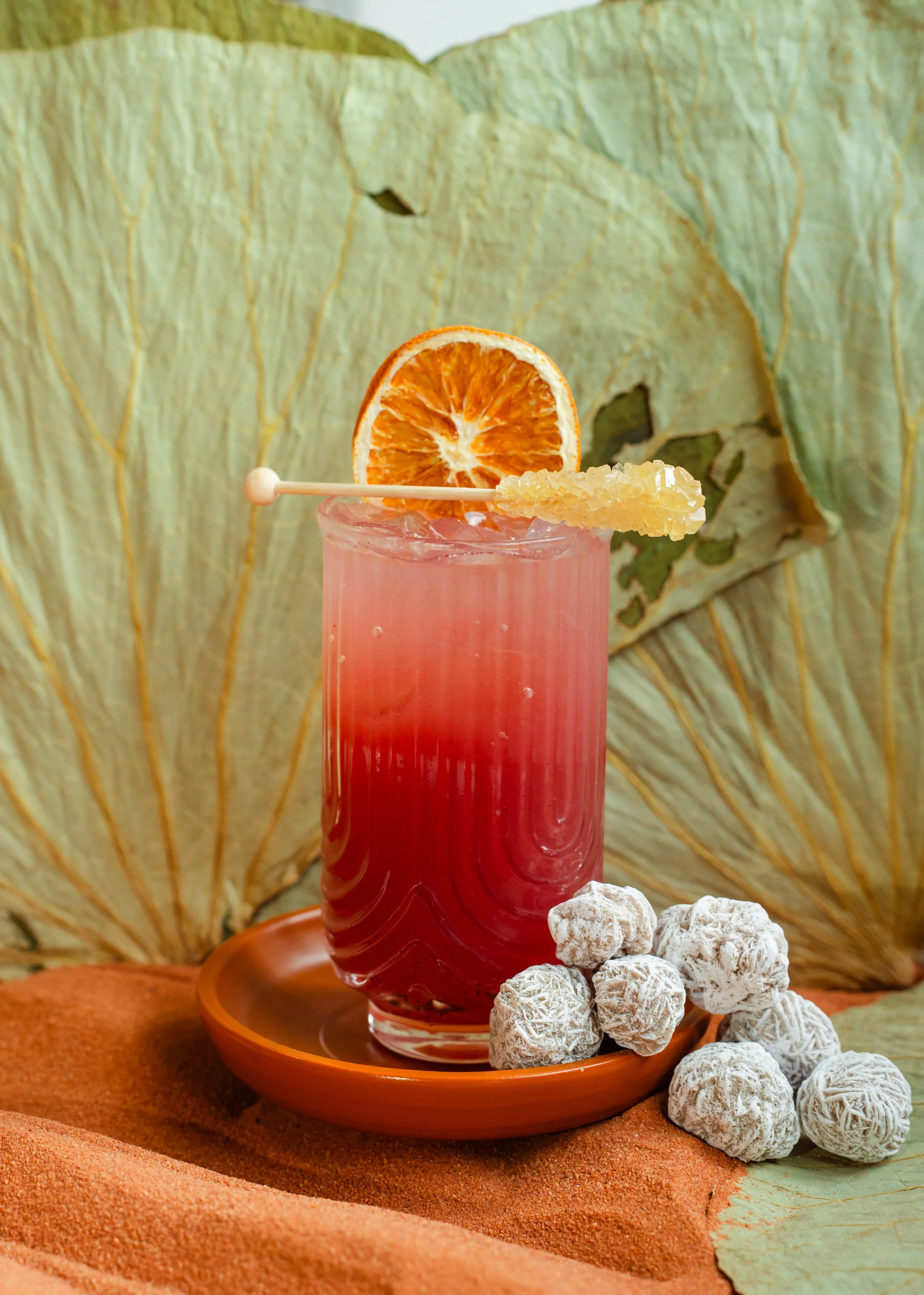 A featured glass with black cherry & prickly pear syrup, vanilla bean, fresh lime juice, and homemade lemonade, topped with a dried orange and sugar rock candy.