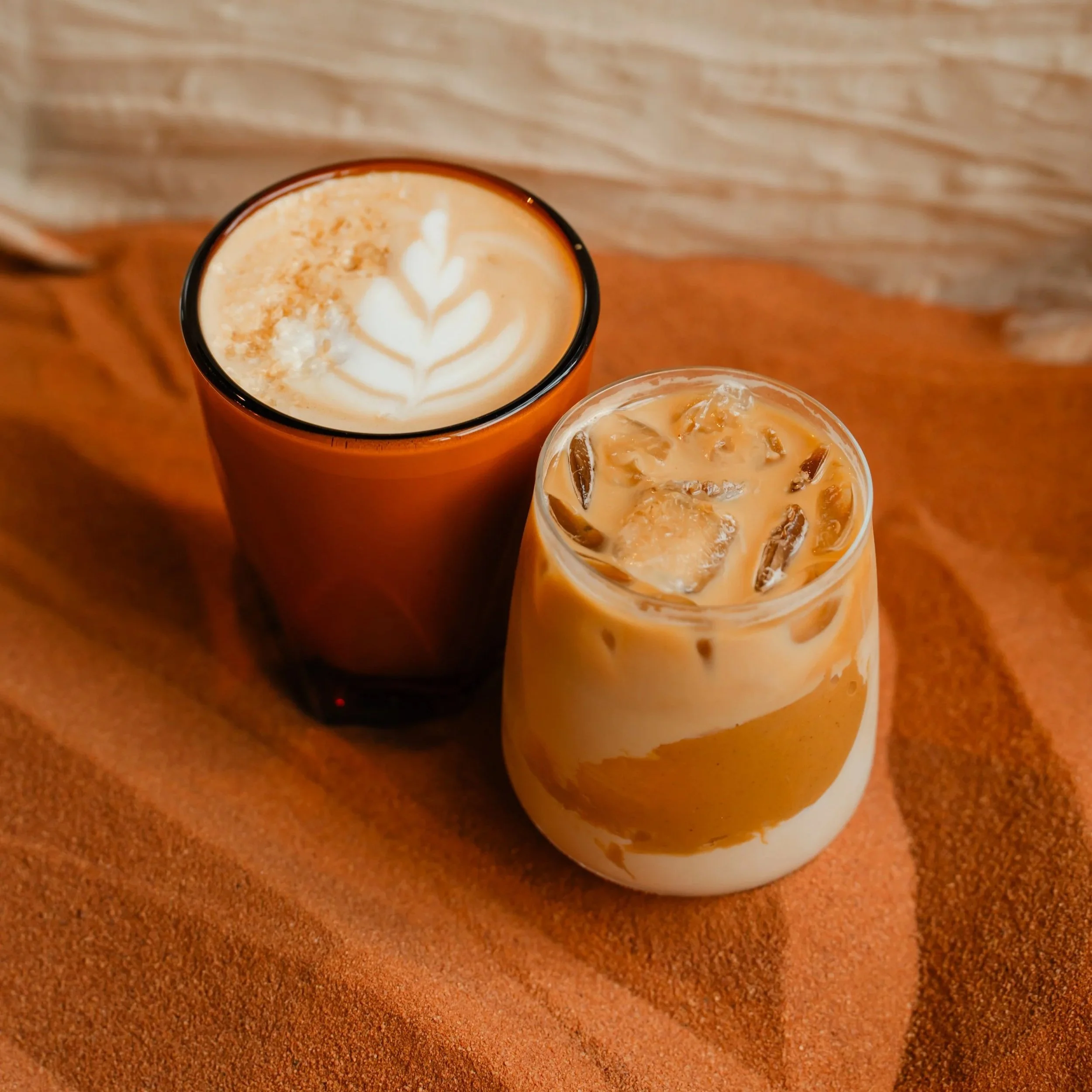 Top view of a salted peanut butter and maple latte with latte art on top, placed on an orange surface with another iced coffee in a clear glass nearby.
