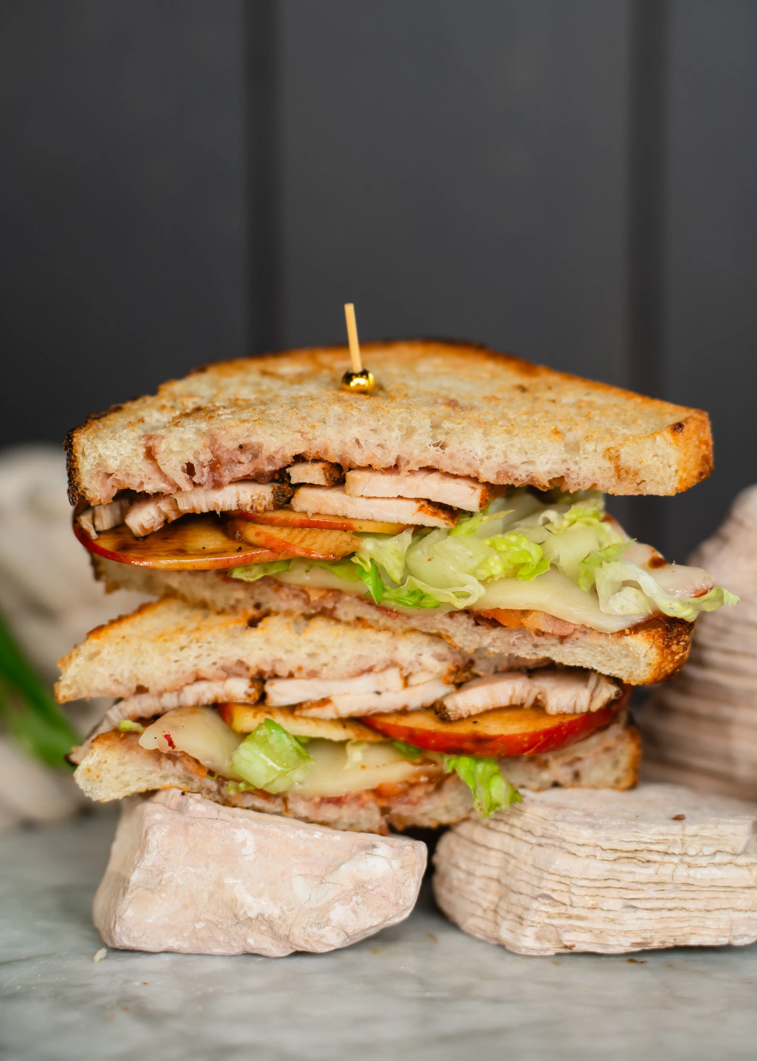 Close-up view of a stacked sandwich with visible layers of bread, turkey, fig spread, honey crisp apples, lettuce, red onion, and balsamic glaze secured with a toothpick.