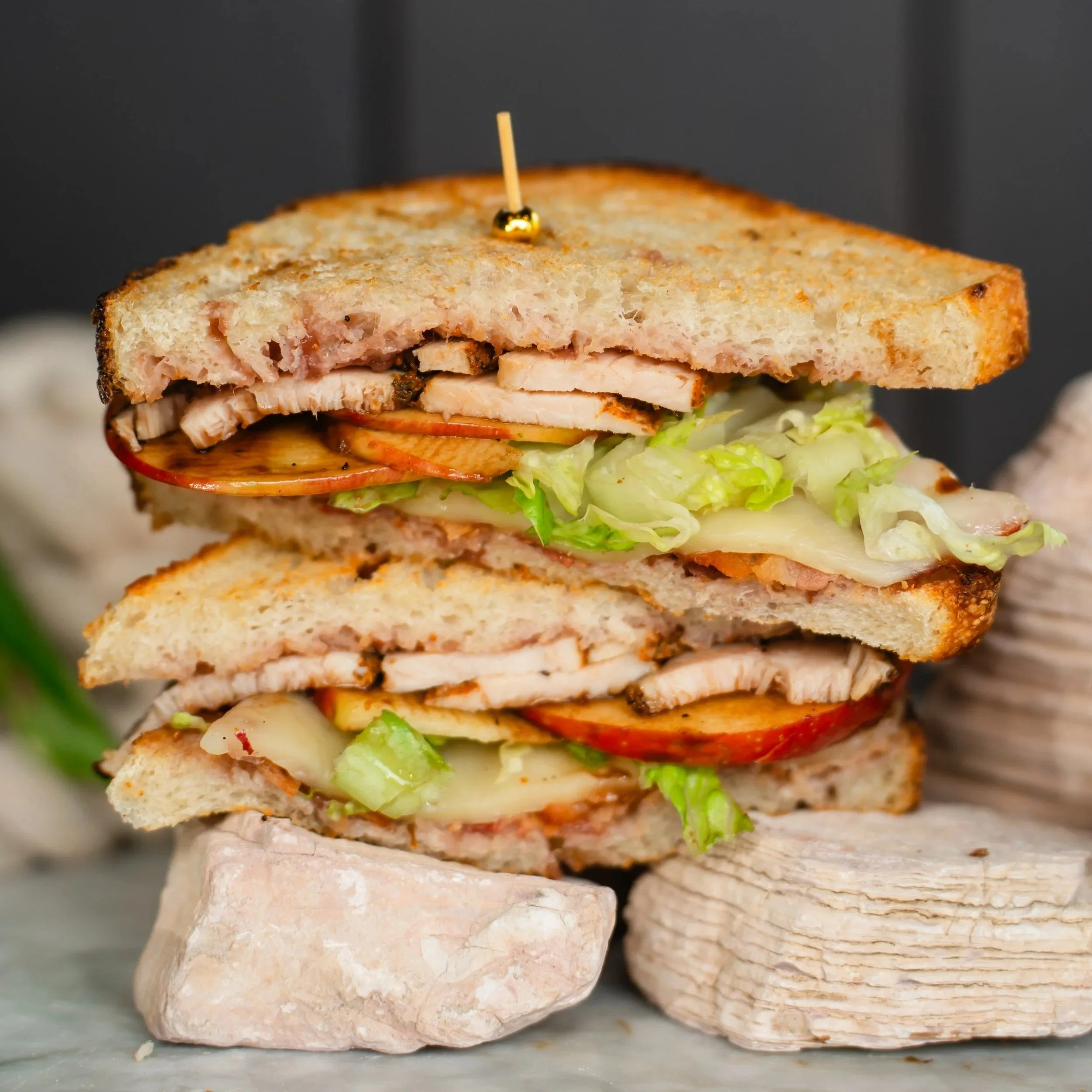 Close-up view of a stacked sandwich with visible layers of bread, turkey, fig spread, honey crisp apples, lettuce, red onion, and balsamic glaze secured with a toothpick.