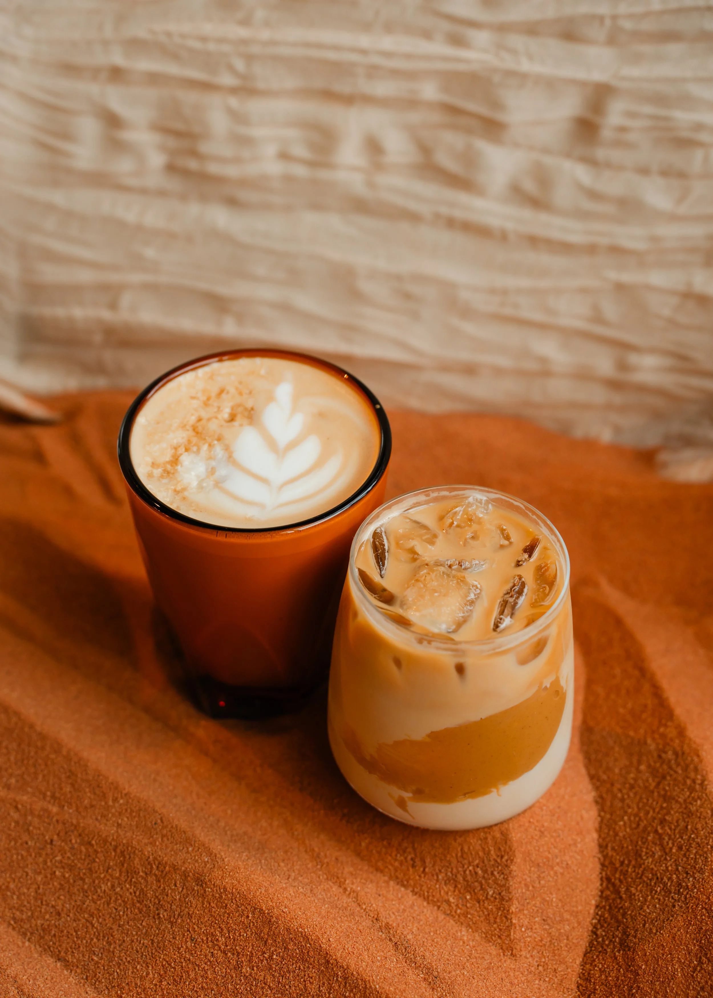 Top view of a salted peanut butter and maple latte with latte art on top, placed on an orange surface with another iced coffee in a clear glass nearby.