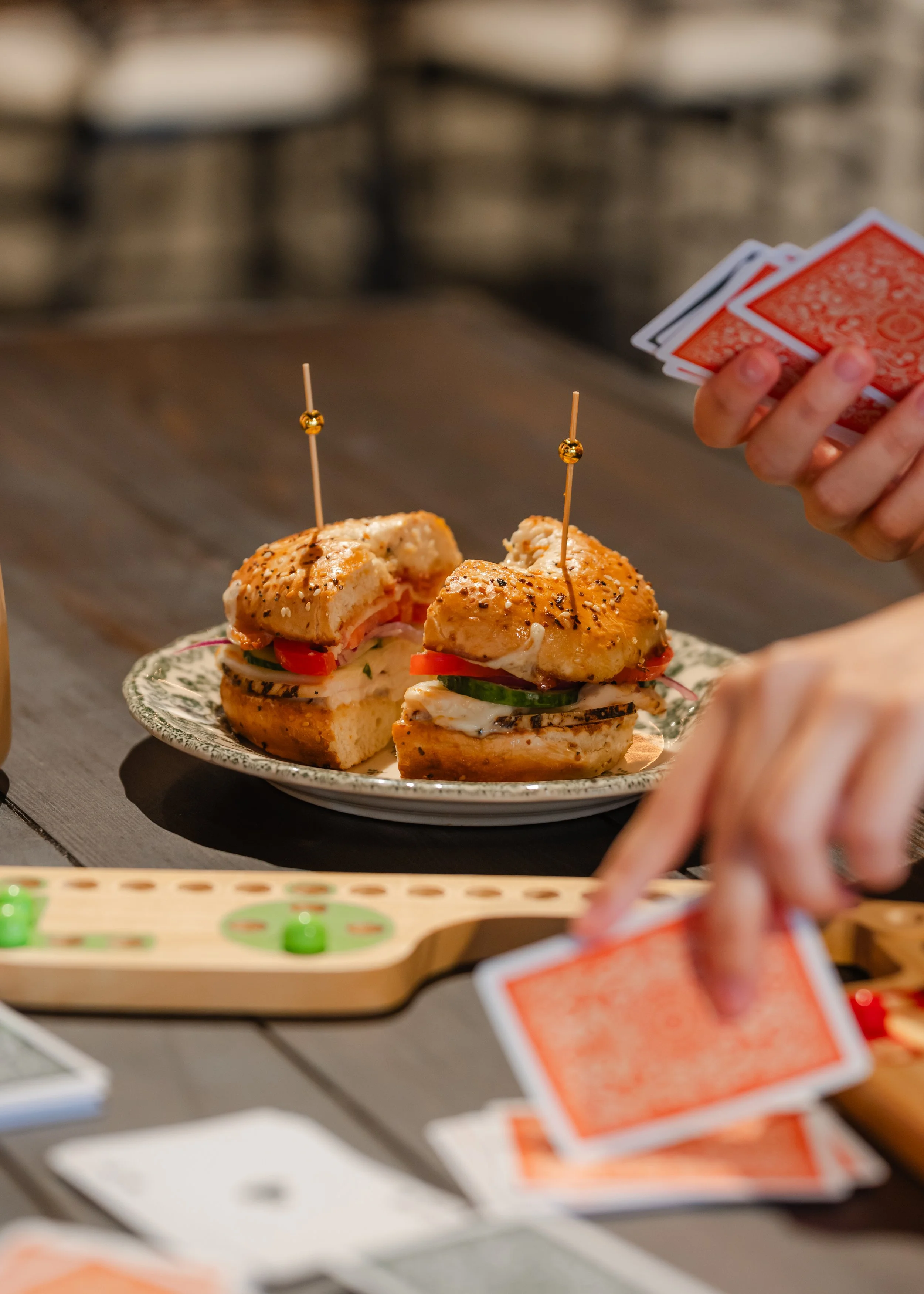 Close-up of a plated sandwich filled with garlic aioli, chicken, bacon, mozzarella cheese, tomato, cucumber, red onion, lemon olive oil on a toasted everything seasoning bagel 