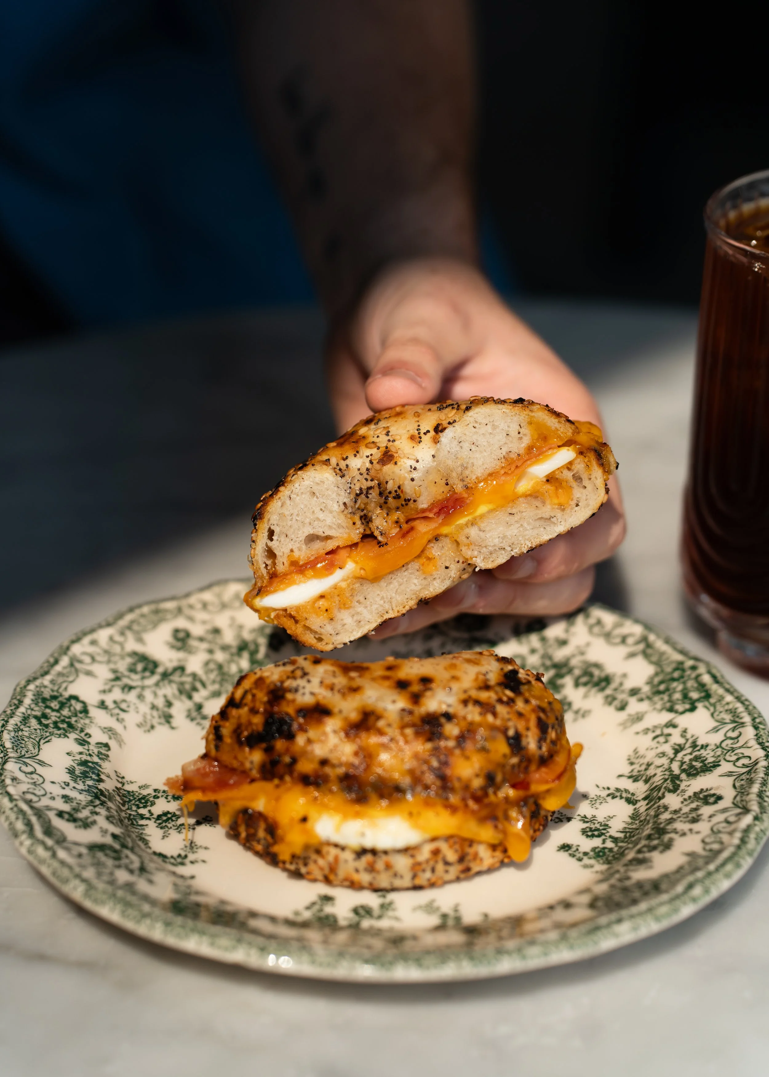 Close-up of a person holding a breakfast sandwich with chipotle ranch, bacon, sliced egg, cheddar cheese, on an everything seasoning gluten free bagel