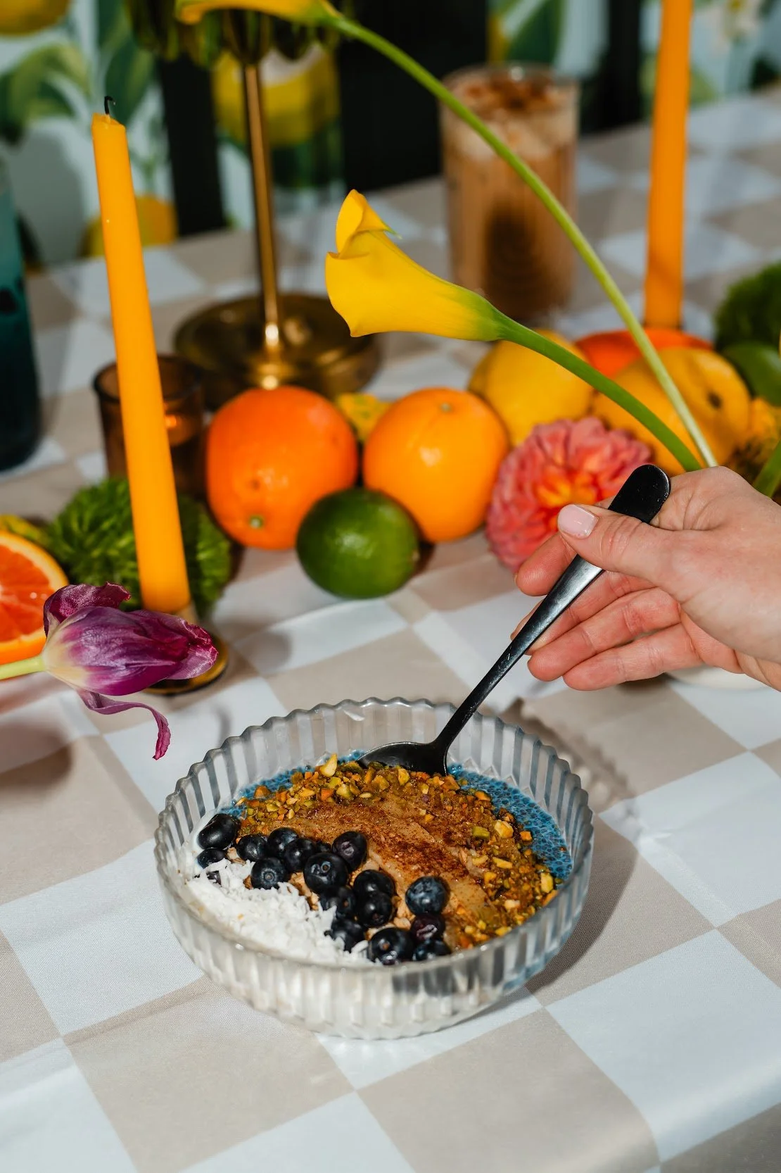 A vanilla yogurt bowl topped with vibrant blue spirulina chia seed pudding, roasted cinnamon-salted banana slices, crunchy granola, fresh blueberries, chopped pistachios, and coconut flakes. The colorful layers and textured toppings. 
