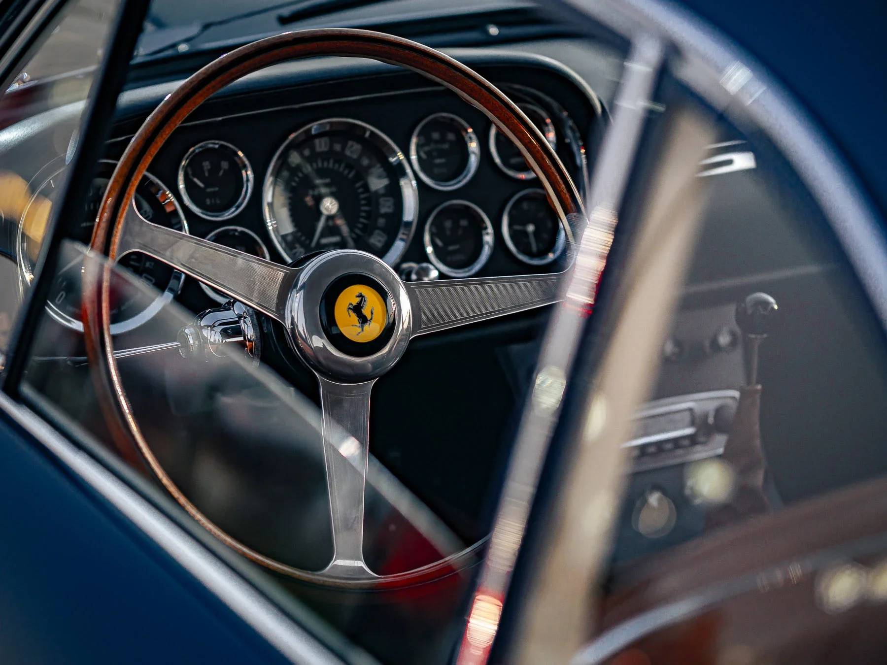Close-up of the steering wheel and dashboard inside a classic Ferrari car, featuring a wooden steering wheel with the Ferrari logo.