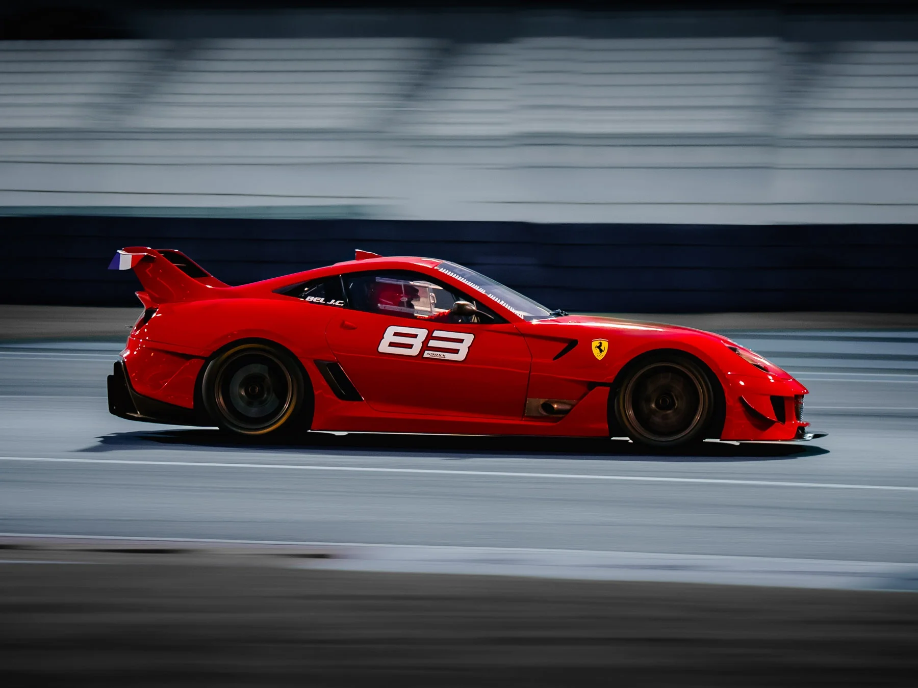 Red Ferrari race car on a track with the number 83 and Ferrari logo, blurred background indicating speed.