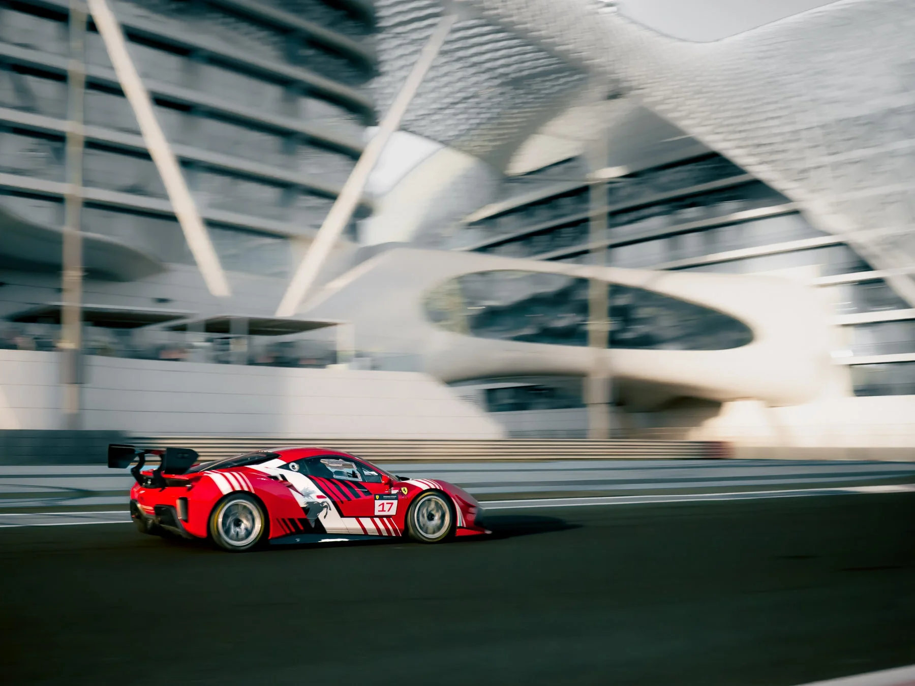 Red race car speeding on a race track with modern buildings in the background.