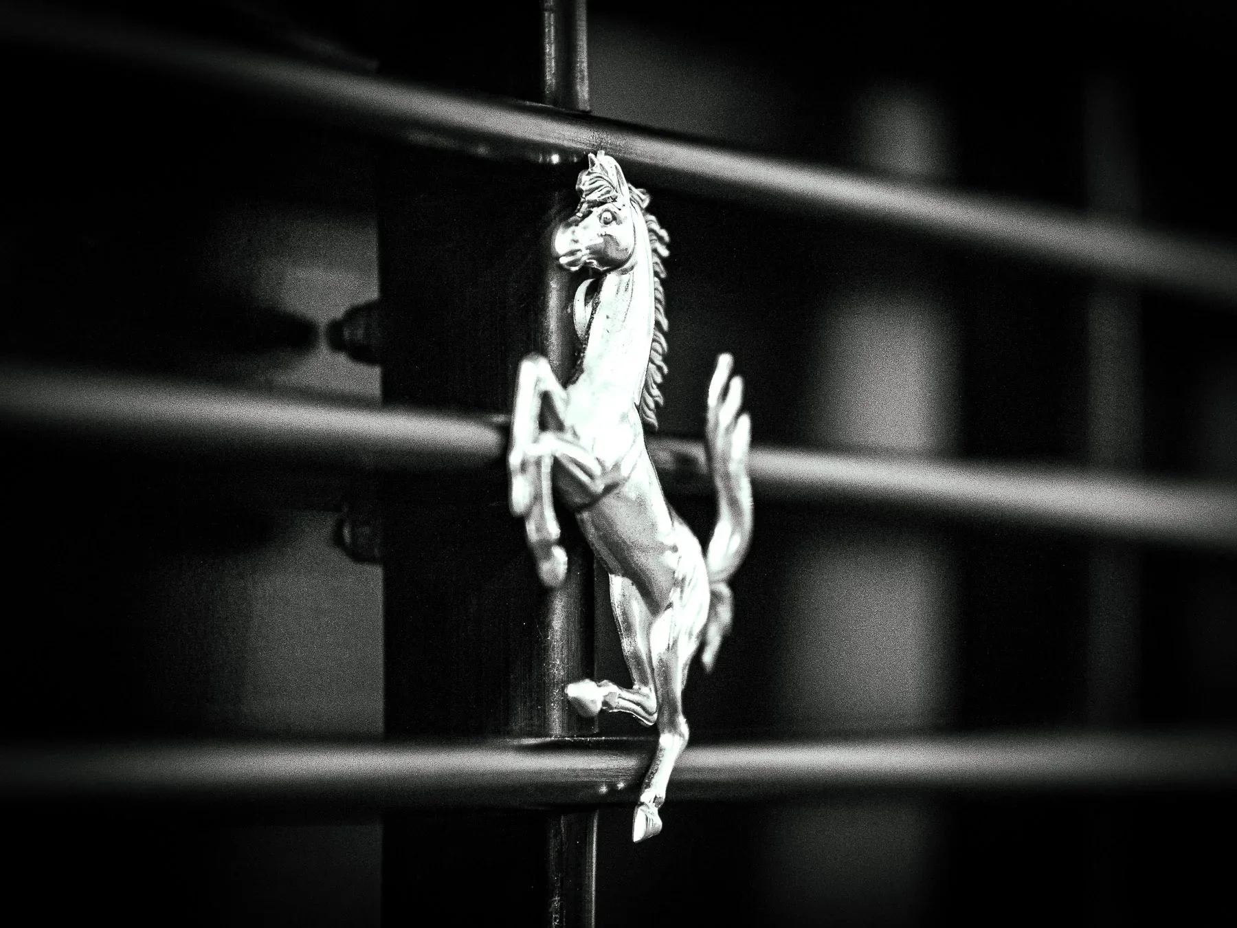 Close-up of a metallic horse figurine attached to a black metal rail, black and white photograph.