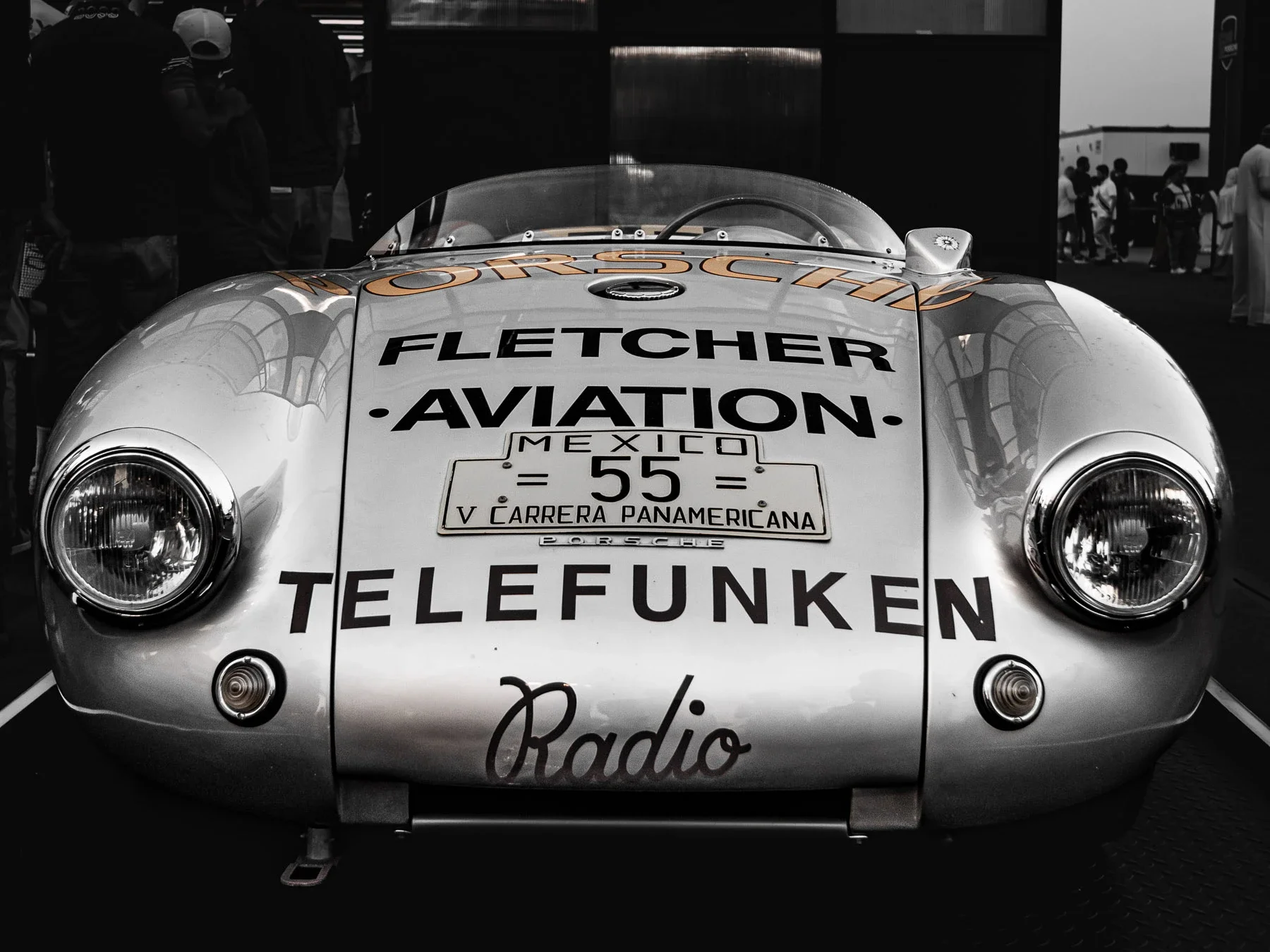 Front view of a vintage Porsche race car with sponsorship decals, headlight details, and a metal body, displayed at a car show.