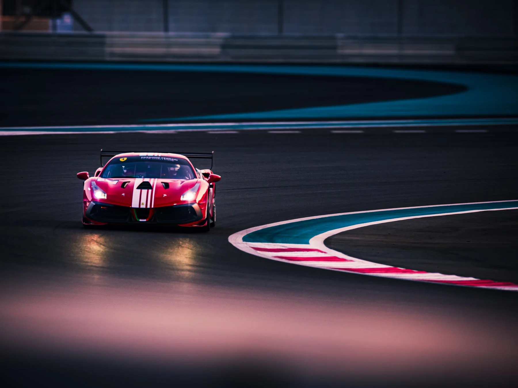 A red race car with racing stripes on a race track during dusk or dawn.