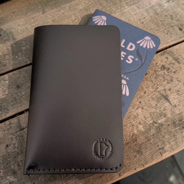 Black full grain leather Field Notes sheath by J.A.B. Leatherworks on rustic wood with a Field Notes notebook.