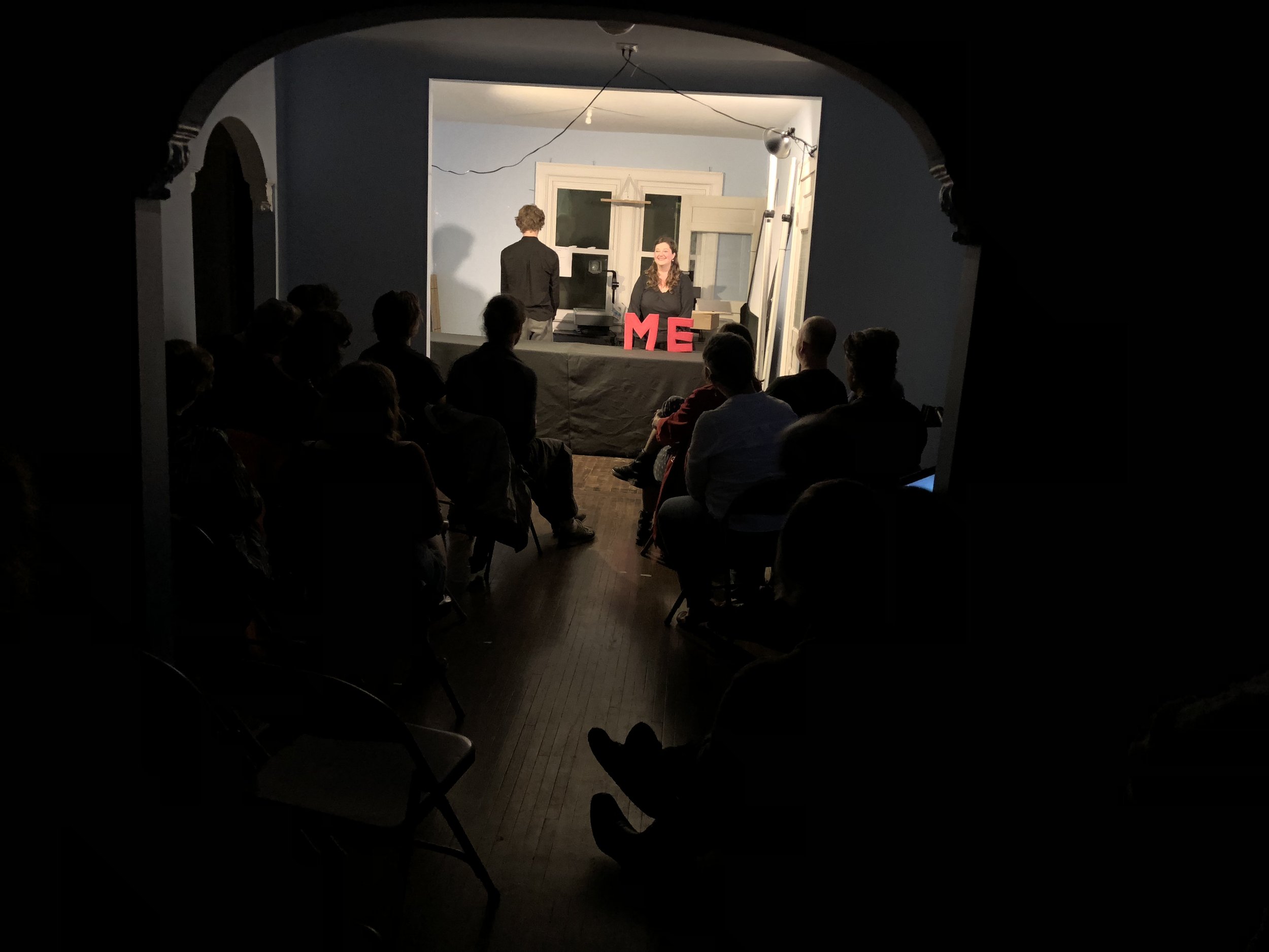 An audience seated and watching an indoor table-top performance.