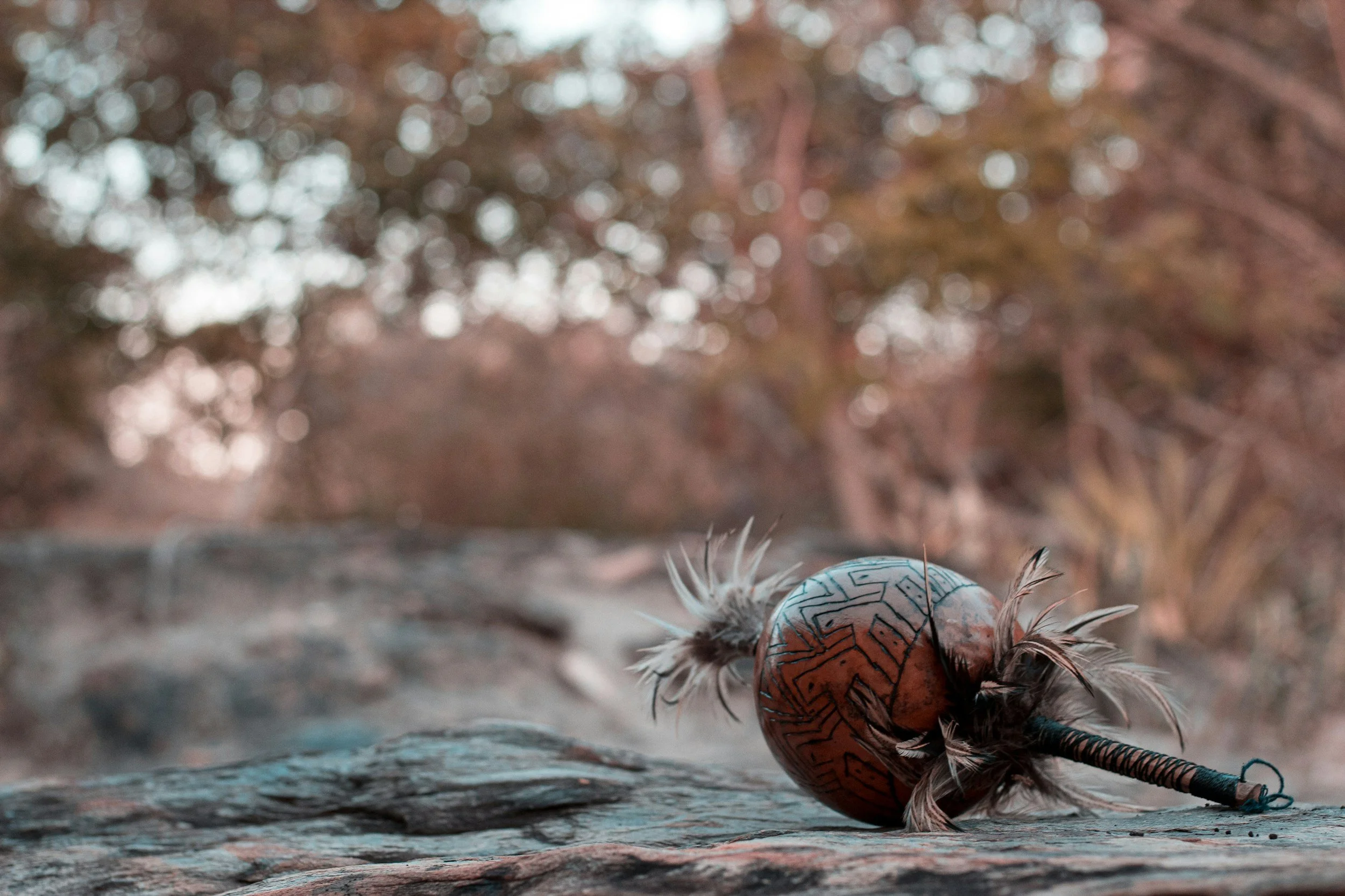 A decorated Mexican-style egg with traditional patterns and feathers resting on a textured surface with a blurred autumnal background.