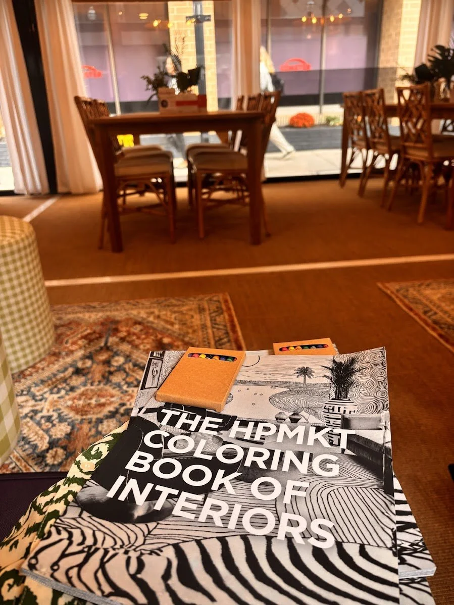 A wooden table with a magazine titled 'The HPMKT Coloring Book of Interiors' and various informational pamphlets and business cards, including one for The Point on Commerce, with green plants in the background.