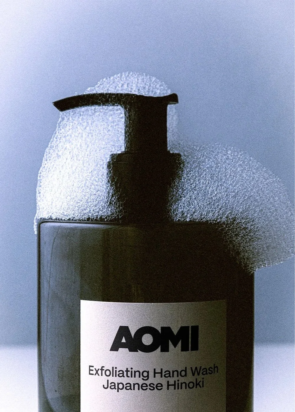 Eine Flasche mit AOMI Exfoliating Hand Wash Japanese Hinoki, Schaum und Seifenreste auf der Flasche.
