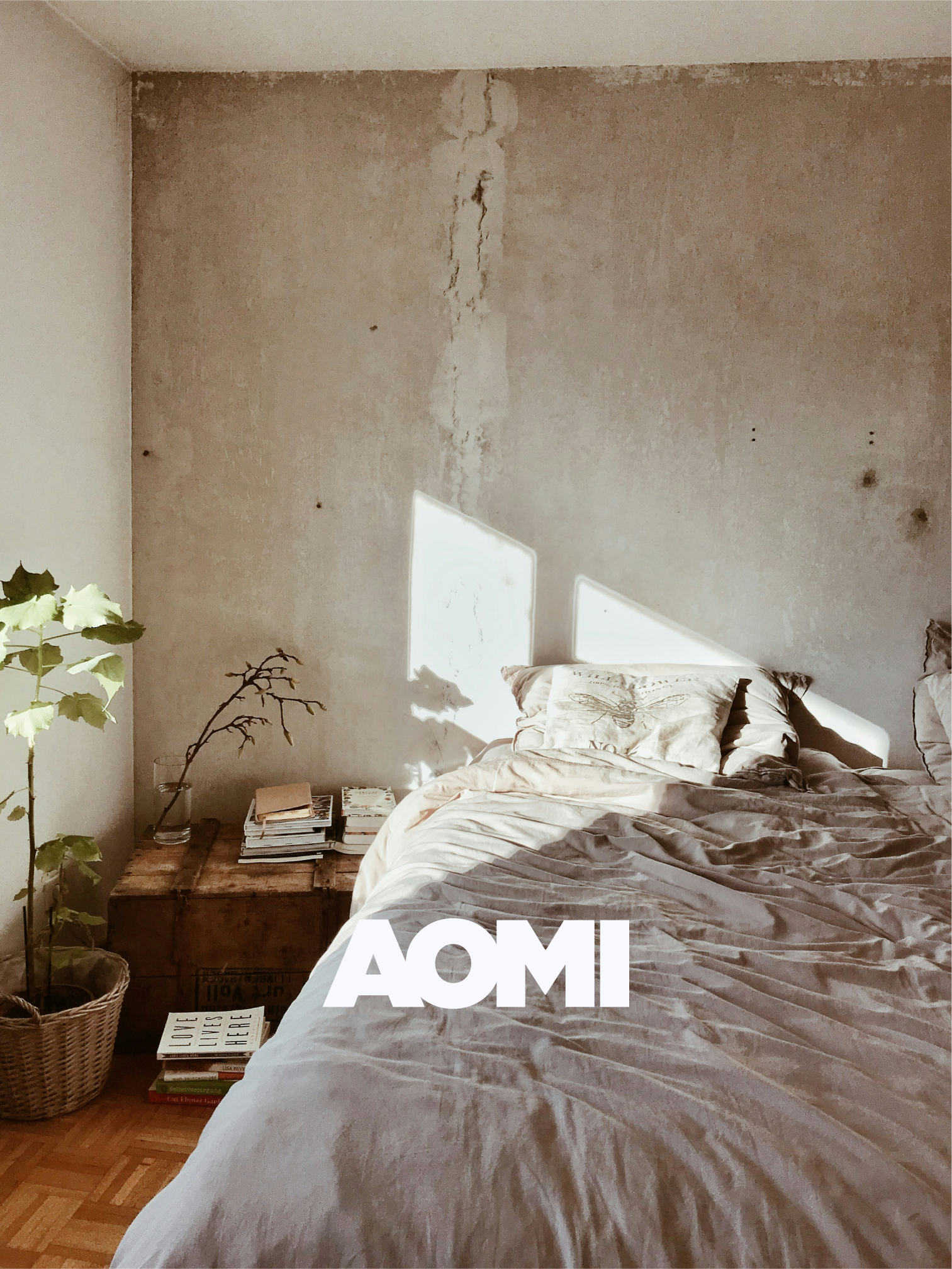 Ein Schlafzimmer mit einem unordentlichen Bett, einer kleinen Nachttischlampe, einem Stapel Bücher und Zeitschriften auf einem Nachttisch, eine Pflanze in einem Korb, eine Wand mit Rissen und Flecken, Sonnenlicht, das durch ein Fenster scheint.