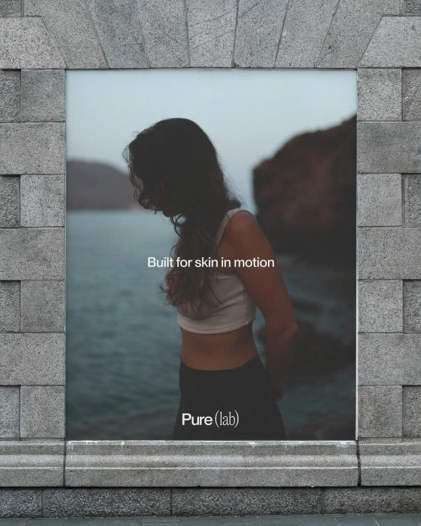 Werbetafel mit einem Bild einer Frau am Wasser, die von einer Felsenwand im Hintergrund umgeben ist, mit Text "Built for skin in motion" und "Purelab"