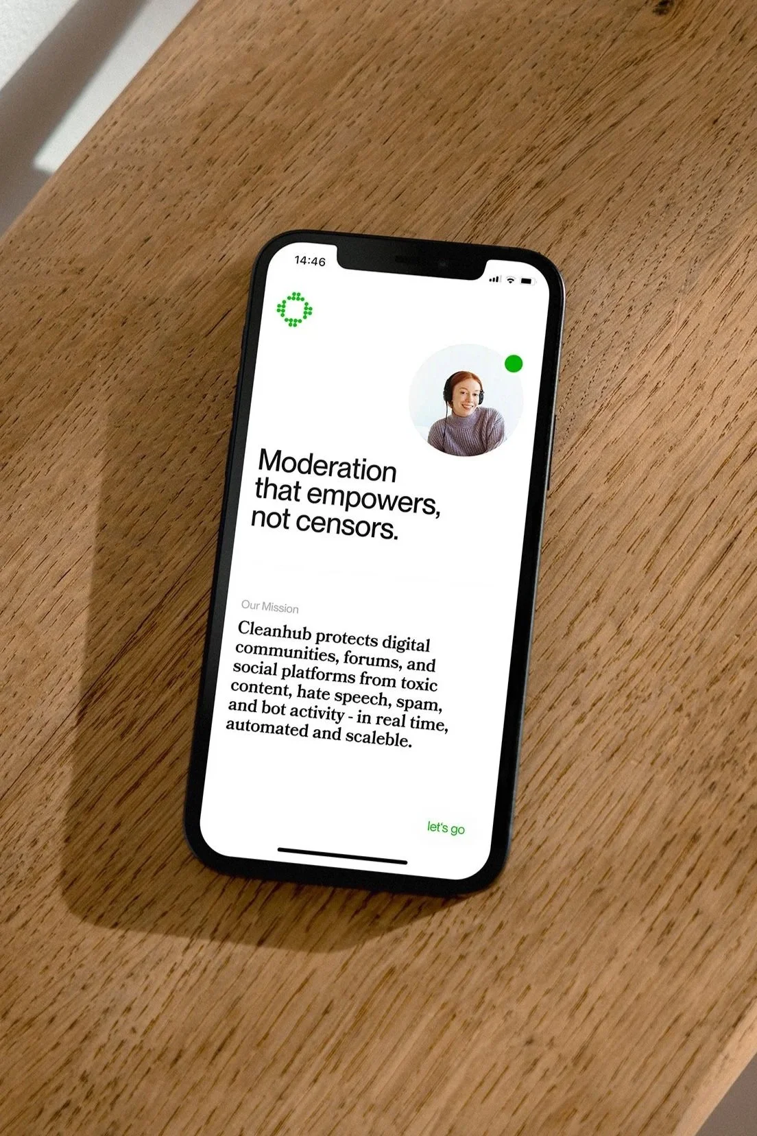 Ein Smartphone auf einem Holz Tisch zeigt eine App mit dem Slogan "Moderation that empowers, not censors" und einer Beschreibung der Mission von Cleanhub, um digitale Gemeinschaften und soziale Plattformen vor toxischem Inhalt und Hassrede zu schützen.