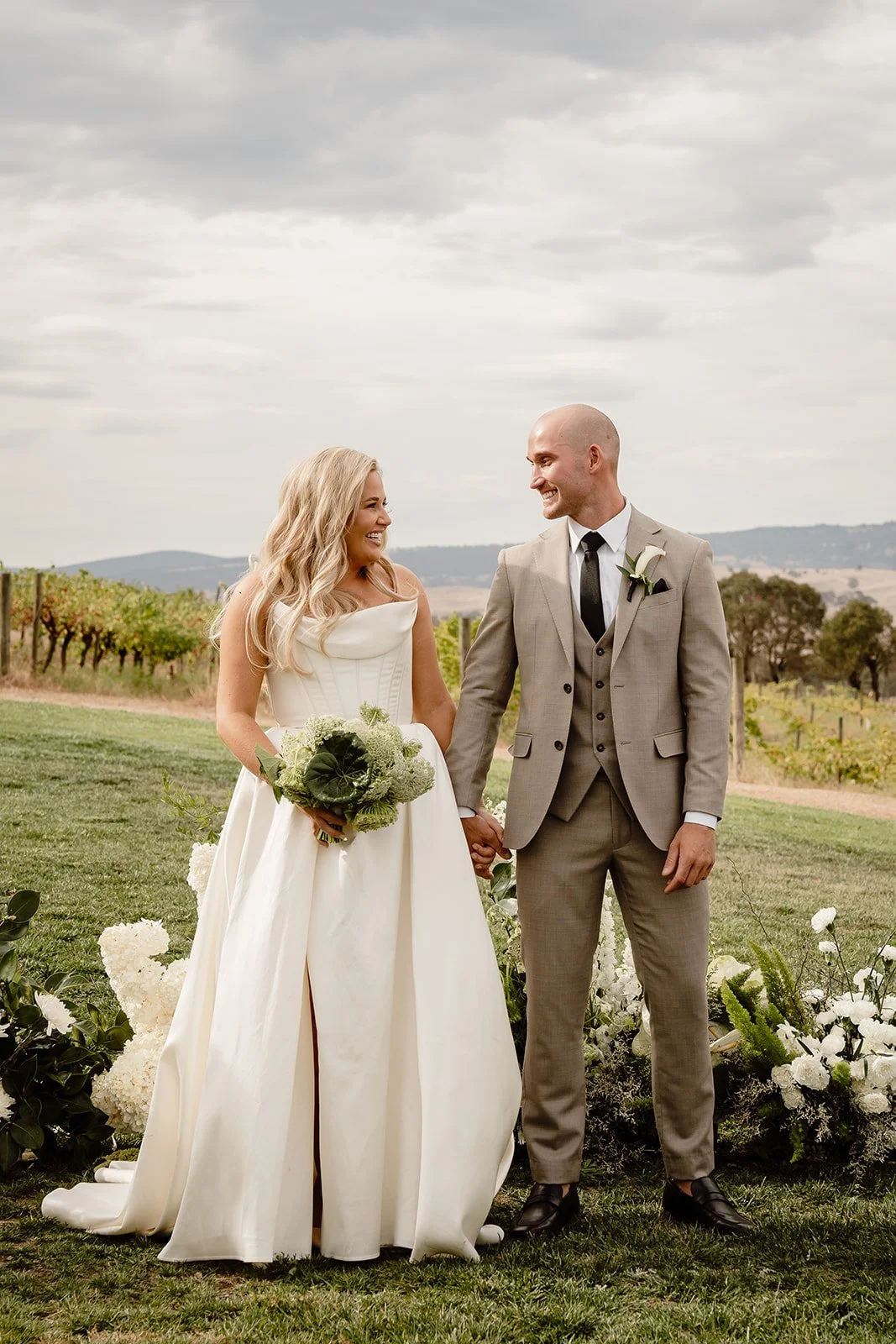 A bride and groom standing in front of their green and white ceremony flowers