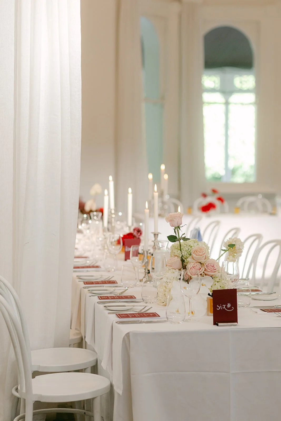 A table with flower arrangements, candles and stationery in burgundy, pink and white