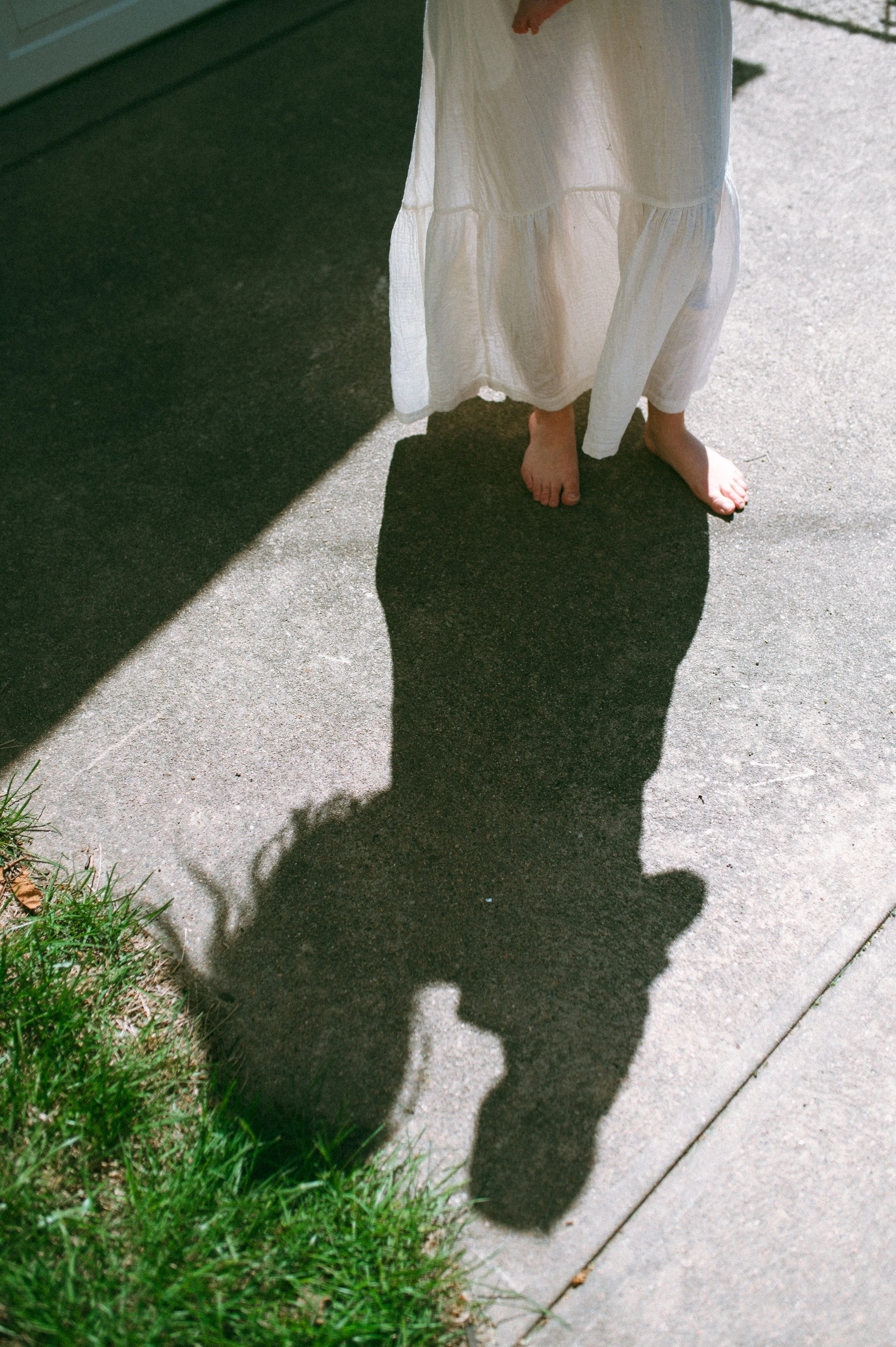 A person's shadow cast on a concrete sidewalk, with a small patch of grass on the left side of the image.