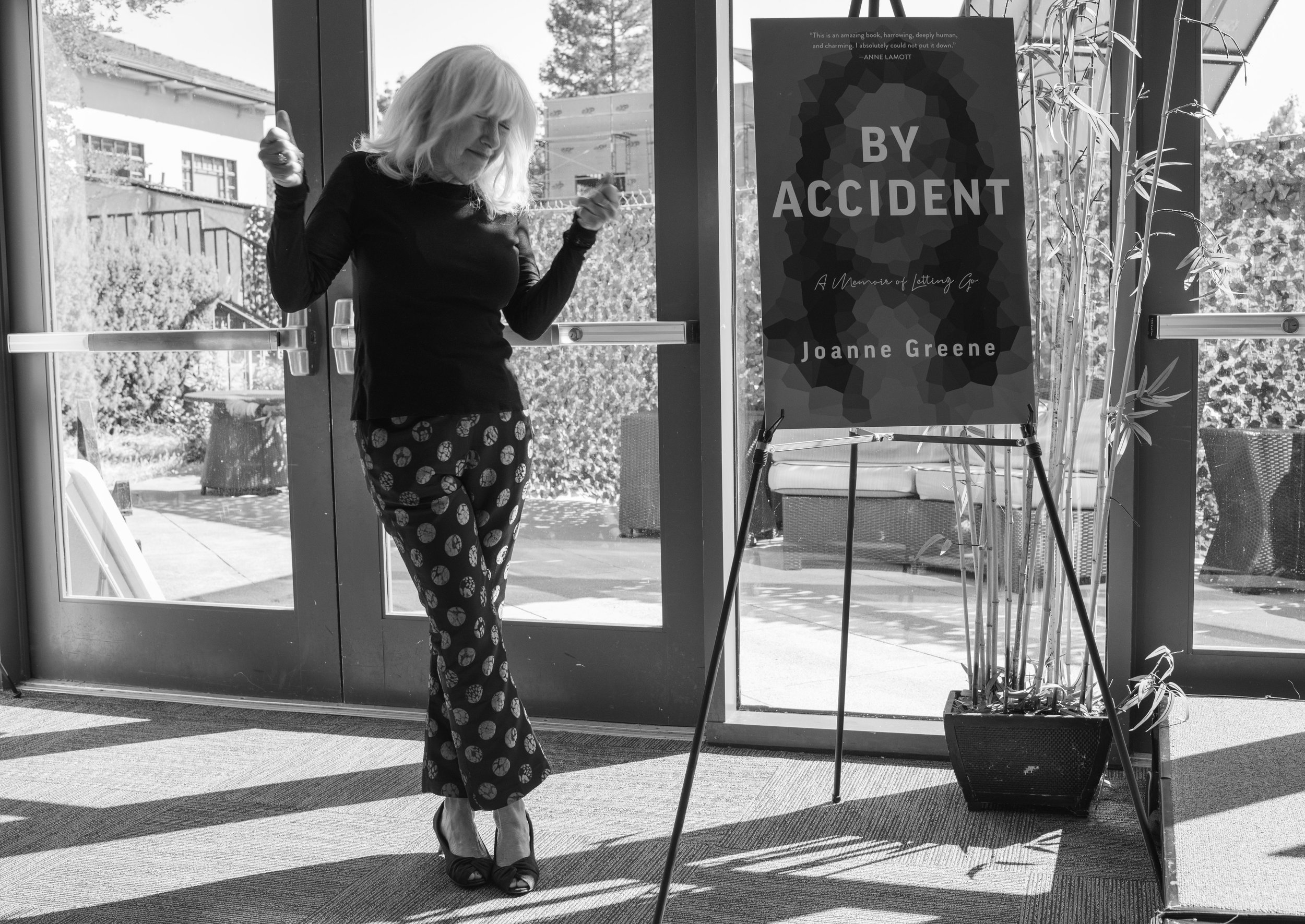 Joanne Greene in black and white dancing in front of a large cardstock display of her book cover By Accident at the Book Launch Event at the Osher Marin JCC..