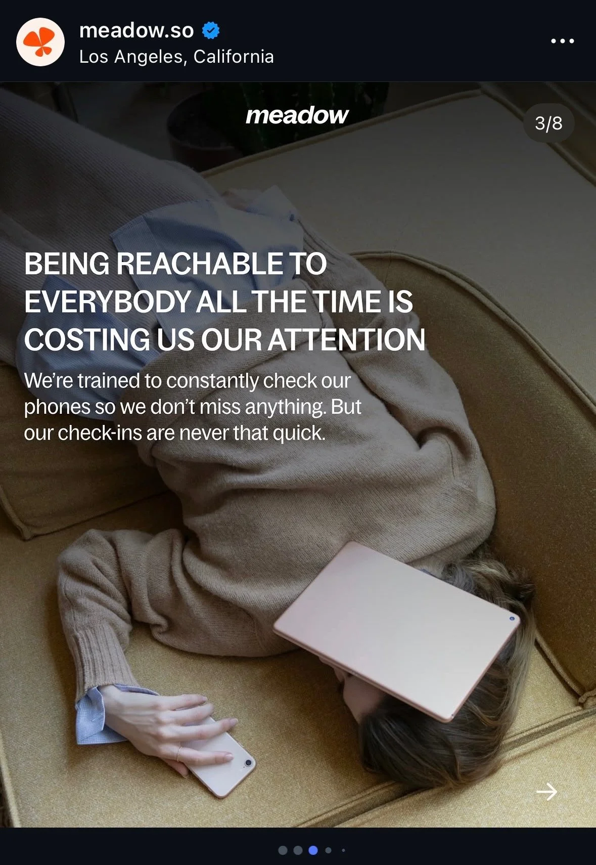 Person lying on their side on a beige couch, with a phone in one hand and a tablet on their face, partially covering their head, in a relaxed setting.