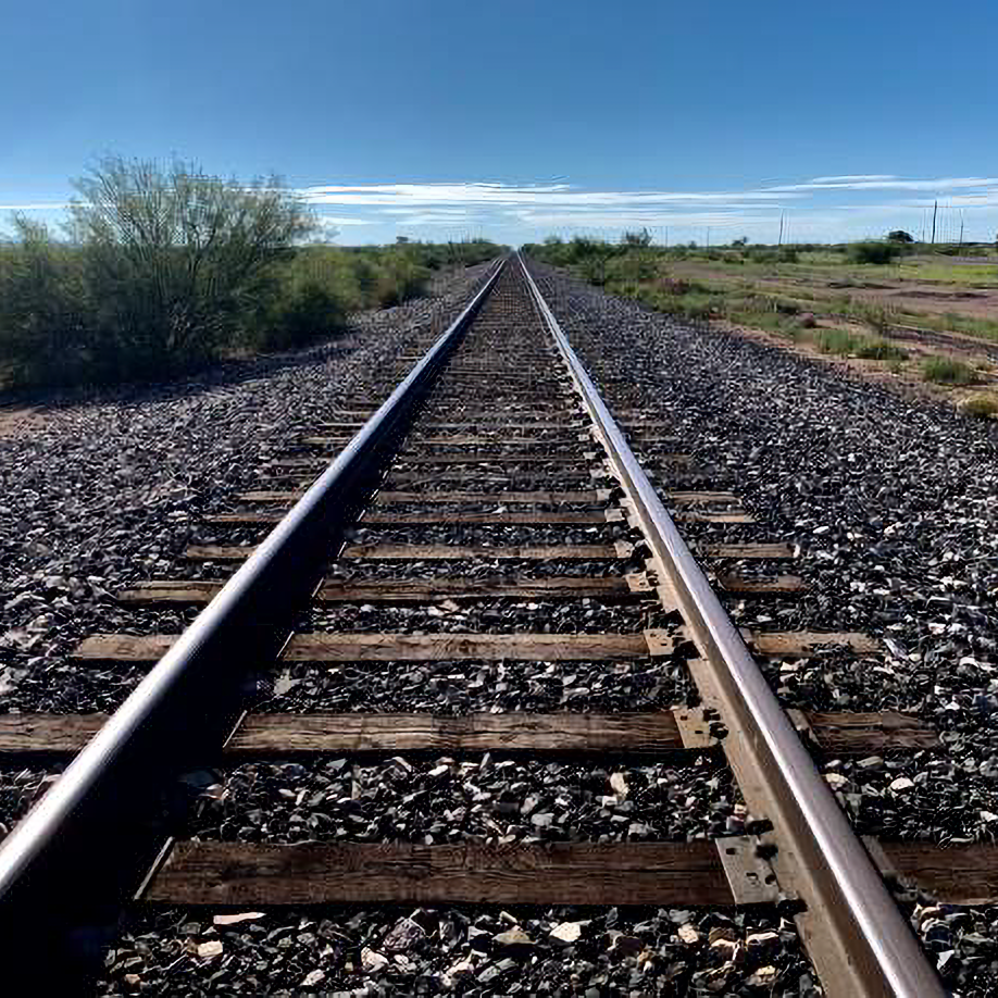 Photo looking down the line on railroad tracks with a blue sky on the horizon.