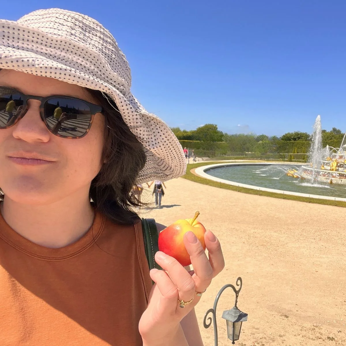 A woman eating an apple at the Versailles Gardens in France