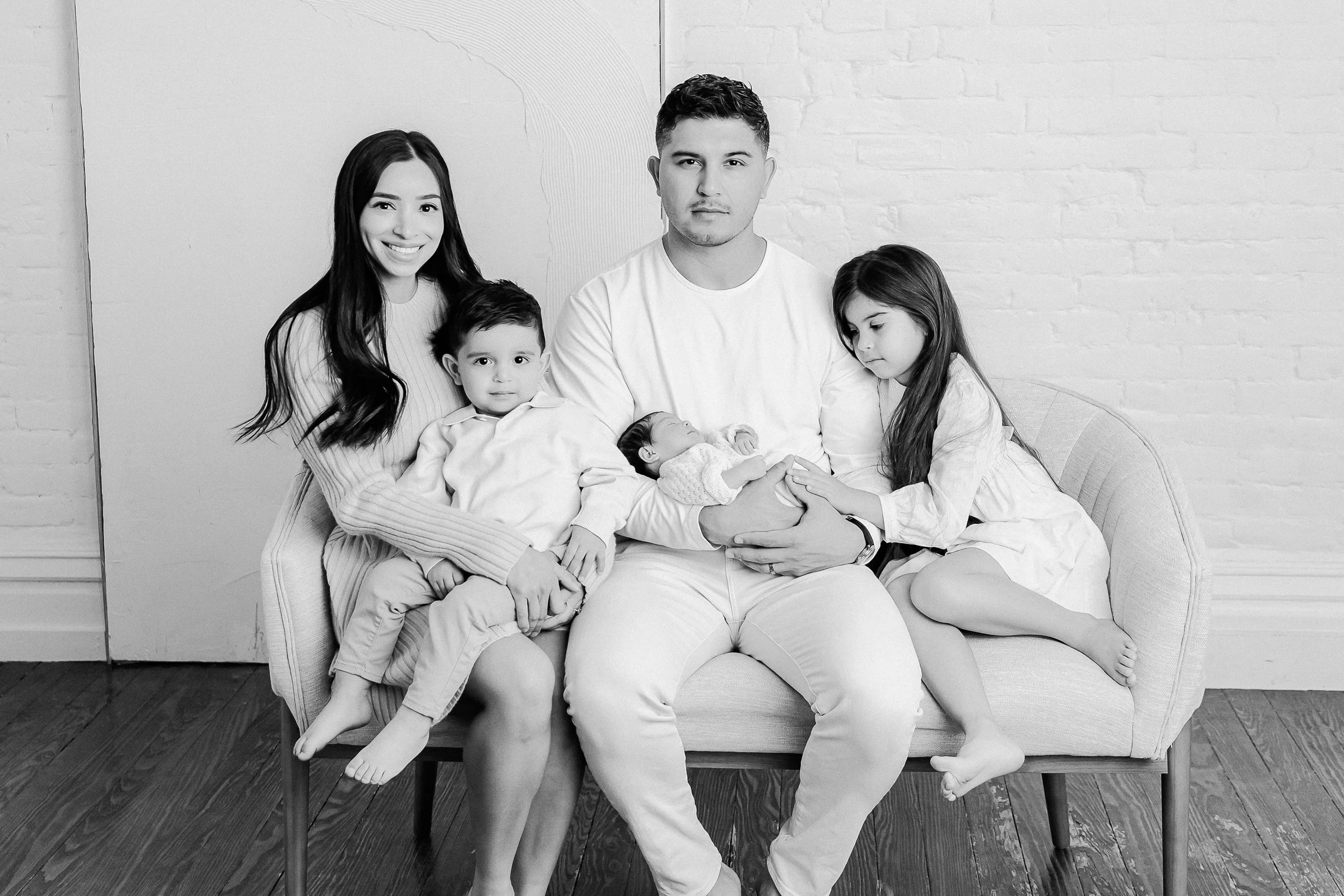 black and white photo of a family of five sitting on a couch with their newborn baby sister