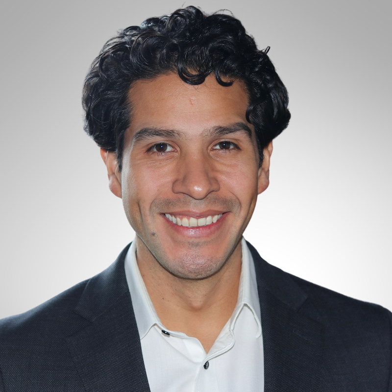 Black and white photo of a Luis Ortega in a suit smiling.