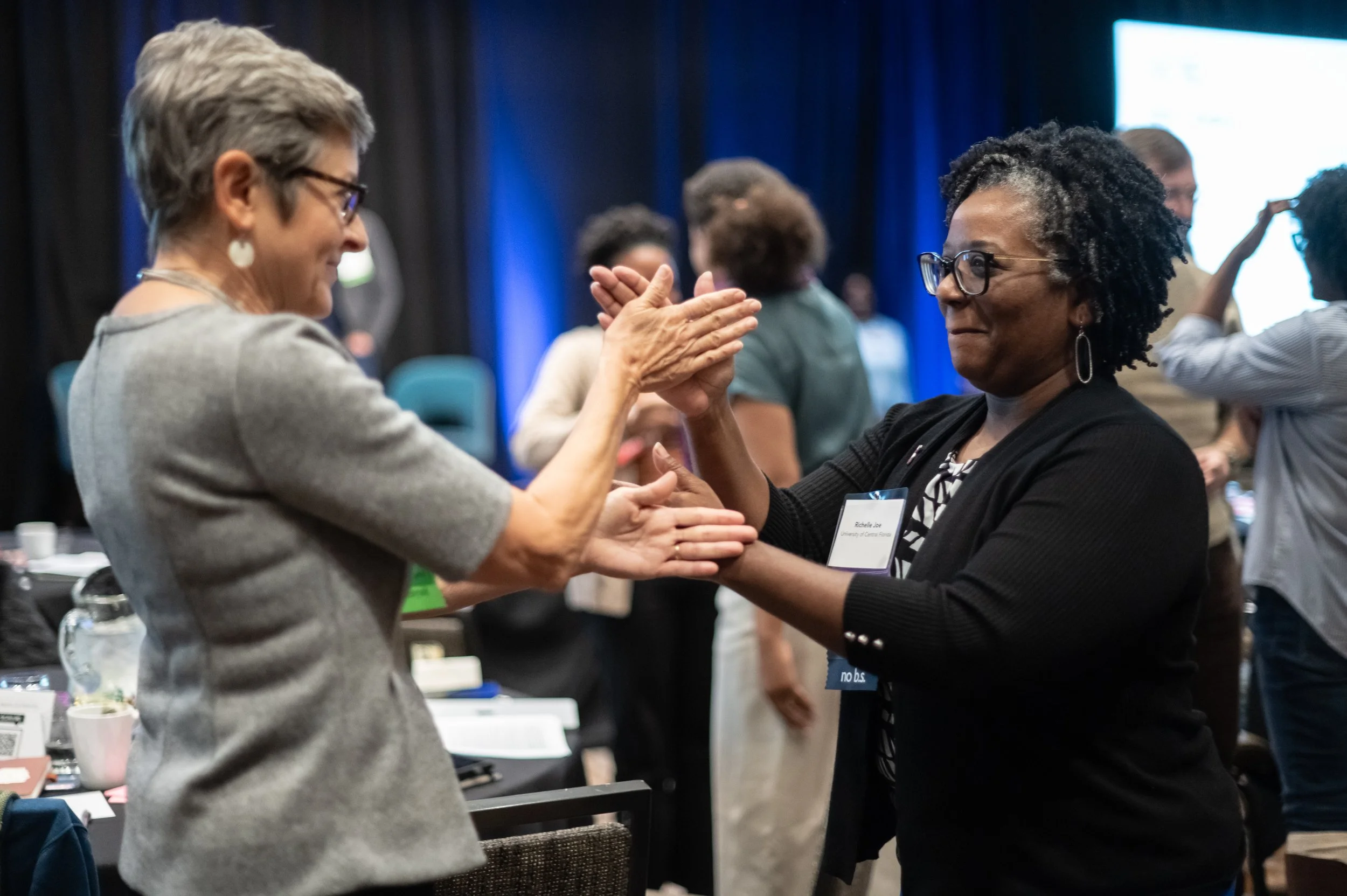 Two women greeting each other with a handshake and high-five at a professional event.