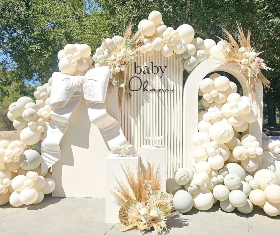 Decorative display with white balloons, white bow, flowers, and the words "baby Omar" in black script.