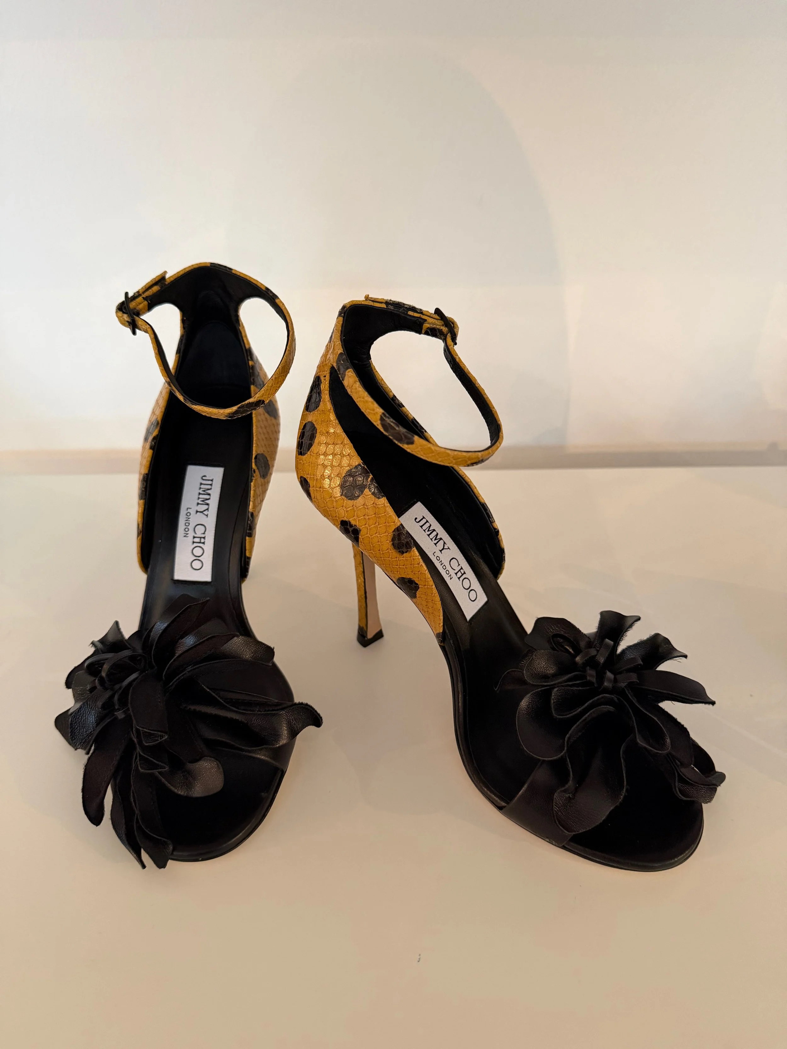 Pair of high-heeled shoes with a leopard print pattern and black satin ribbon ankle straps, displayed on a white surface.