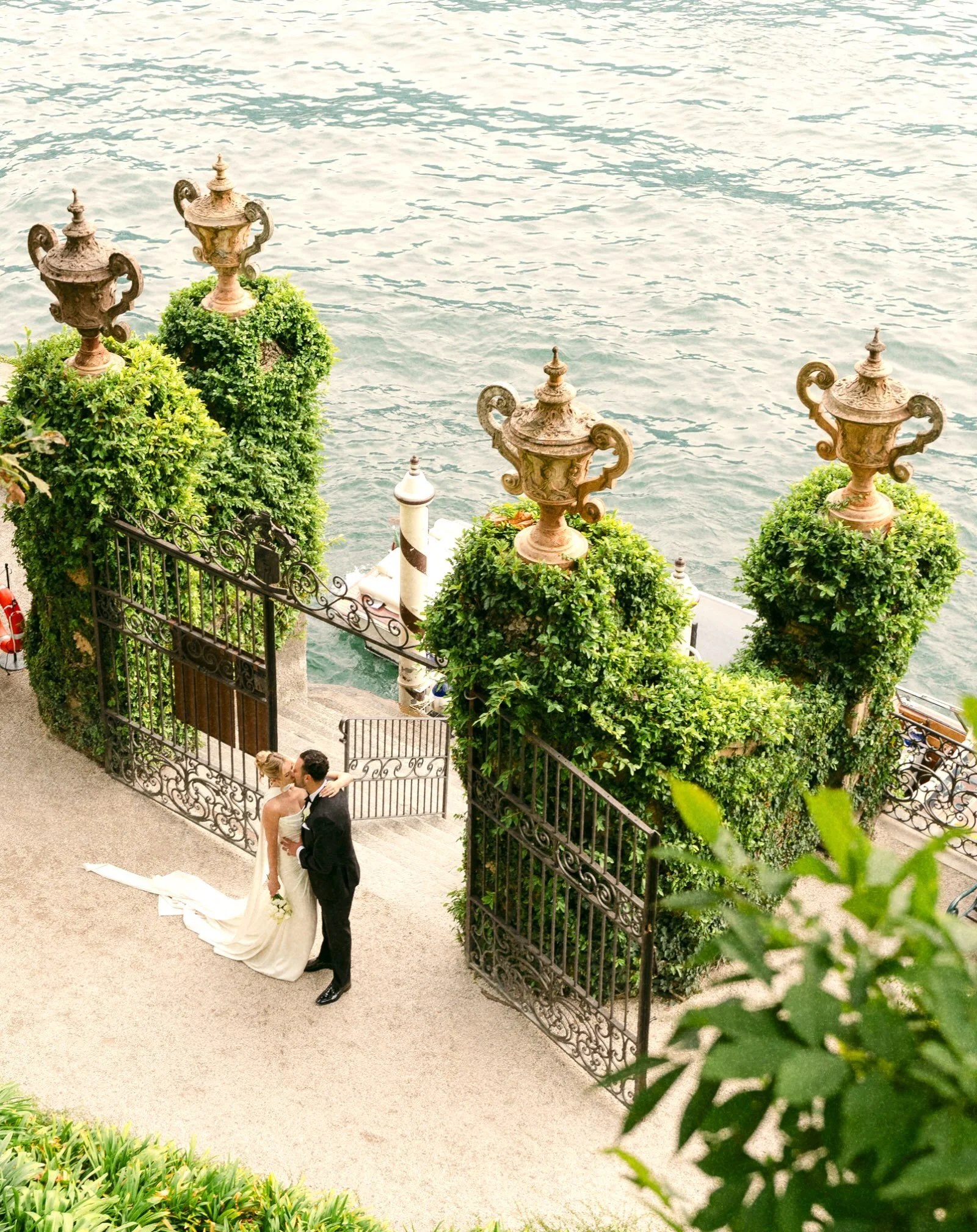 A Lake Como elopement at Villa del Balbianello, a September afternoon, seen from above the water gate.

Four stone urns. Ivy grown thick over the pillars. Iron gates open to the lake, a boat moored at the striped pole below.

No guests to greet, no o
