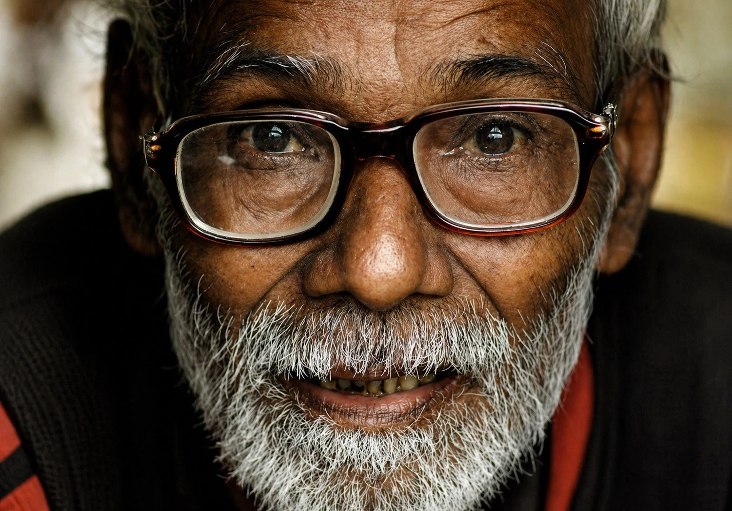 Close-up of an elderly man with gray hair, beard, and glasses, smiling