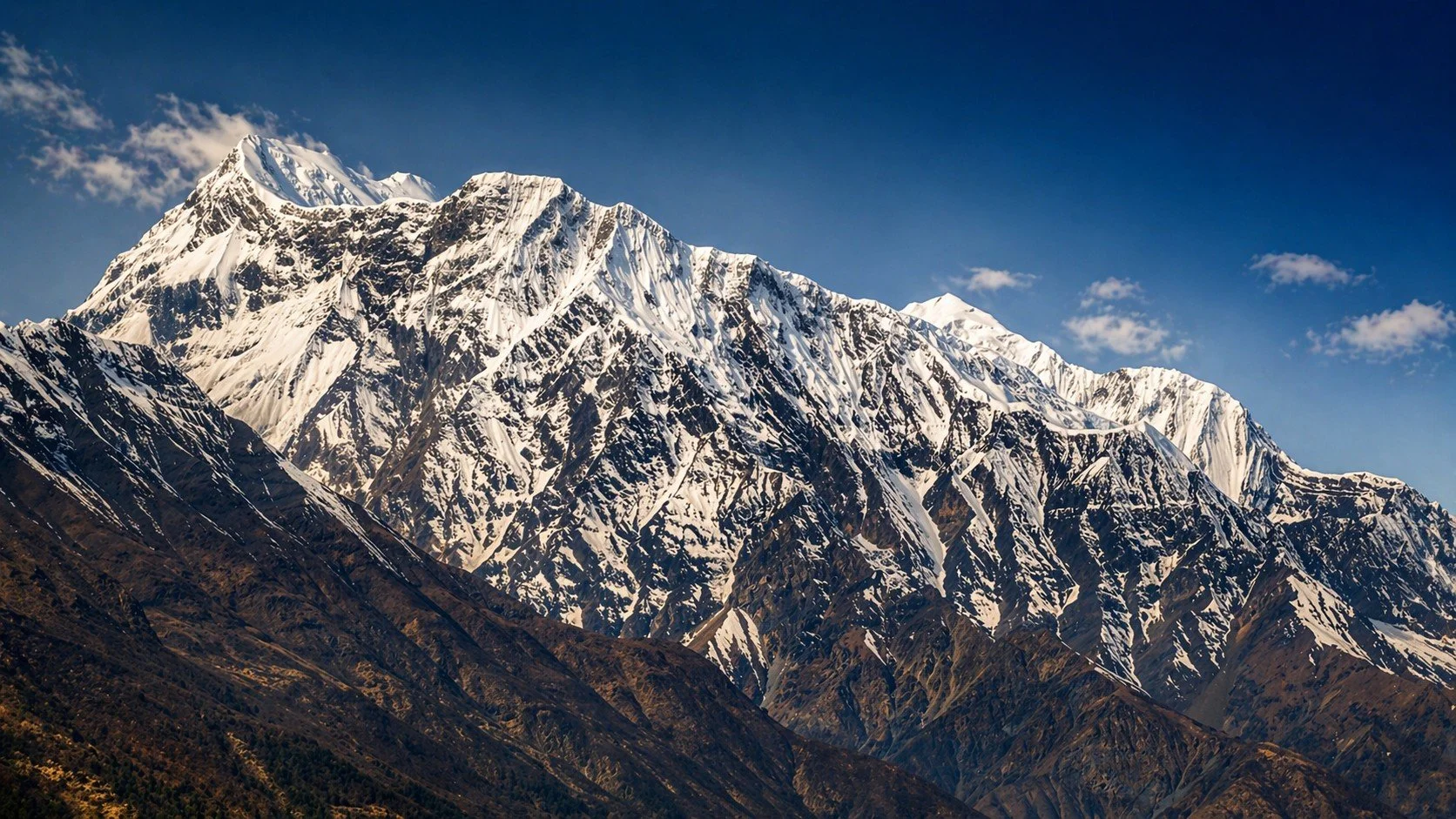 Snow-capped mountains under a clear blue sky with some small clouds.