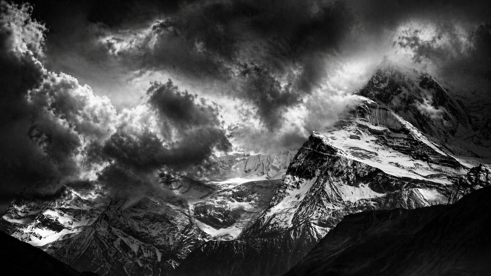 Snow-covered mountain peaks with dark clouds overhead in a black and white landscape photograph.