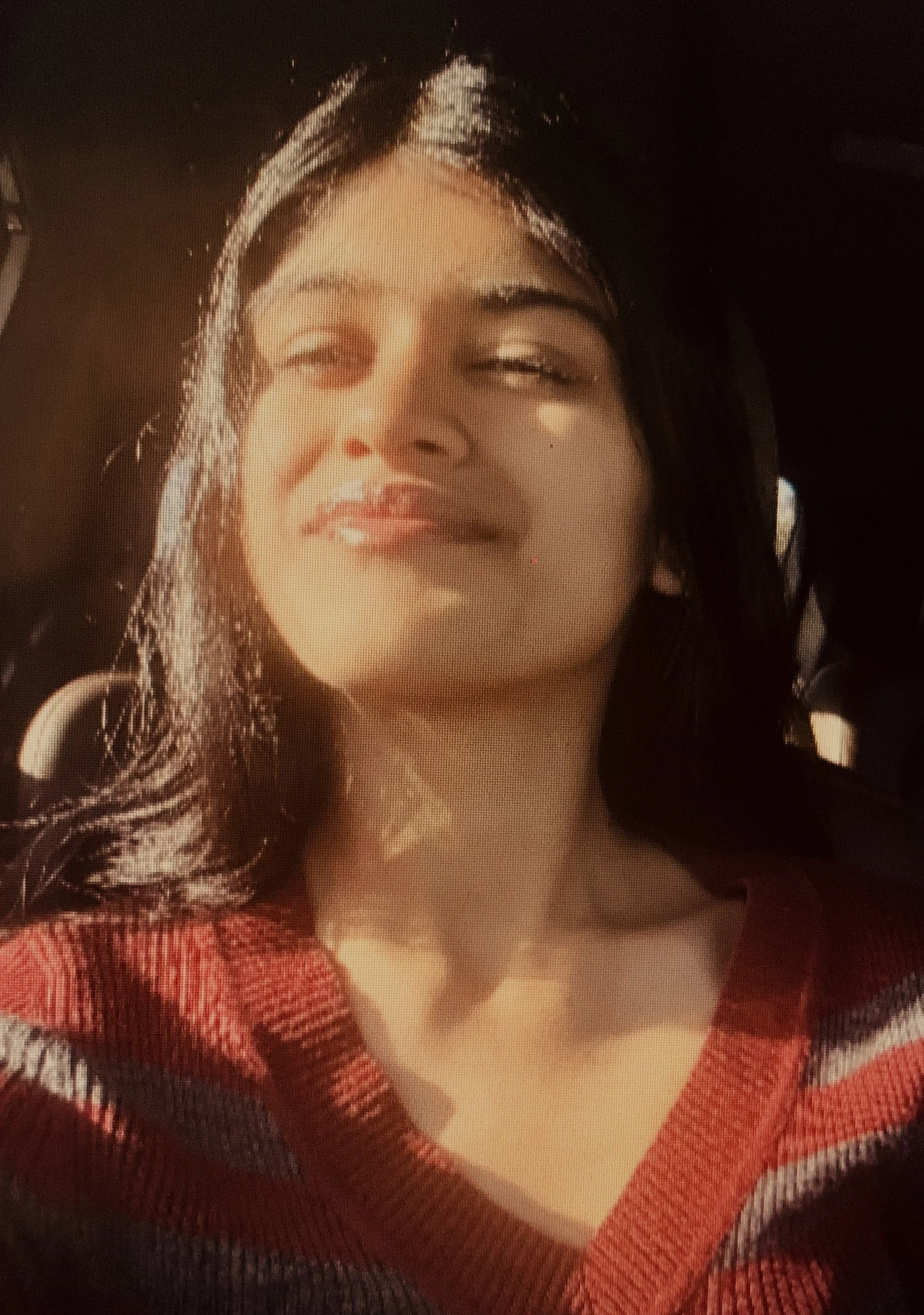 A man in a light blue dress shirt standing outdoors in front of green shrubs and trees with city buildings in the background.